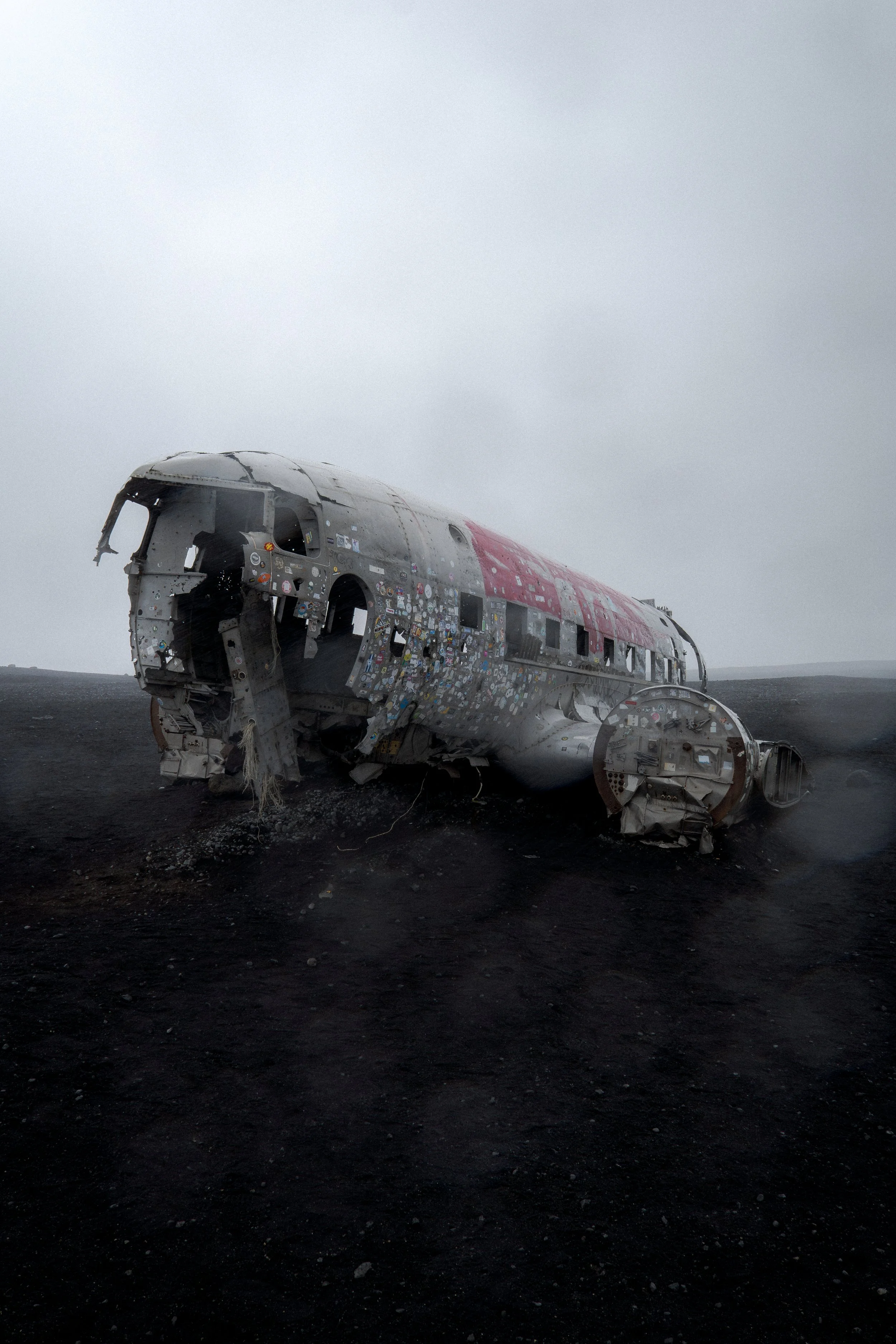 The wreckage of a crashed airplane lying on a barren, dark landscape with a cloudy gray sky.