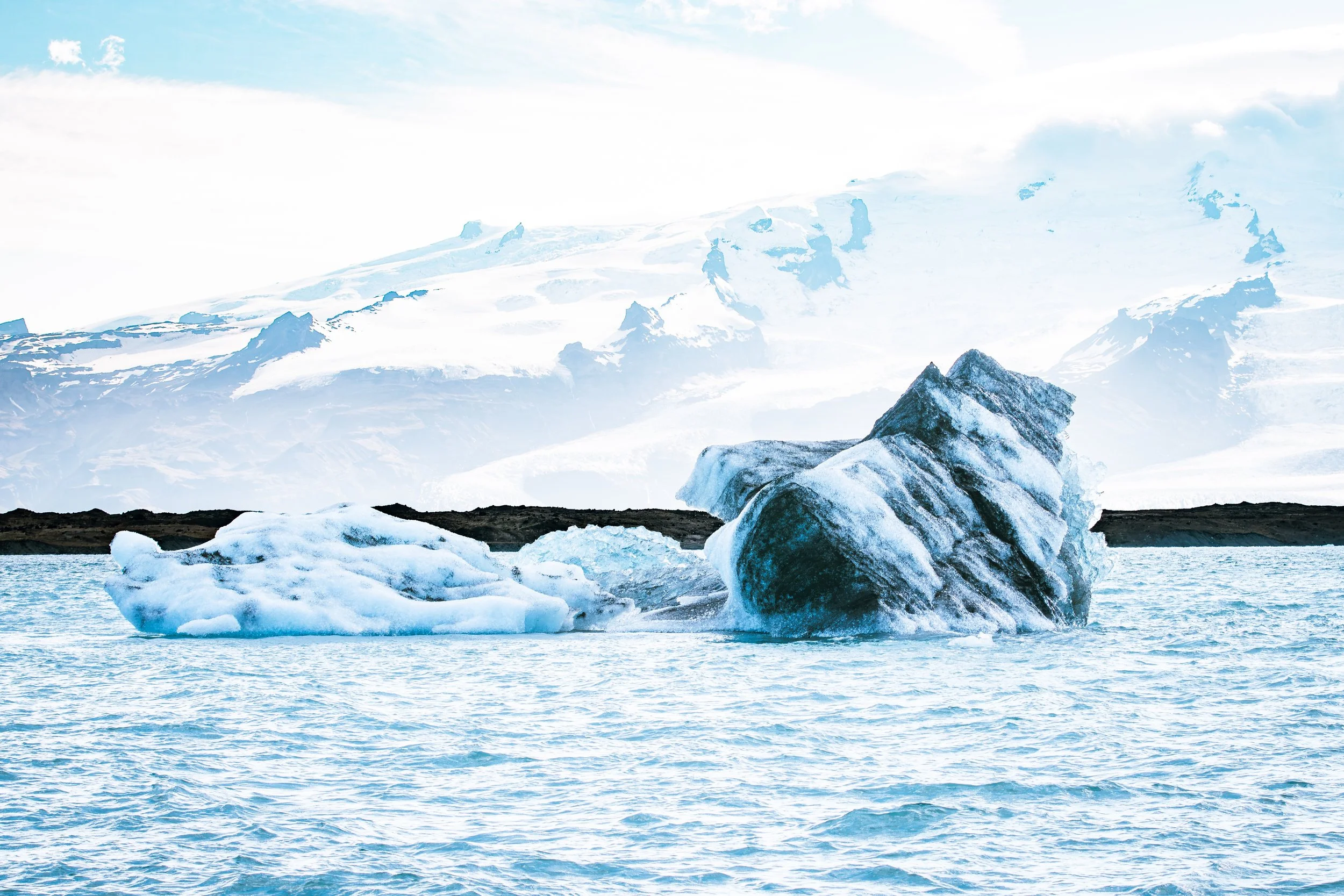 Icebergs floating in a body of water with snow-covered mountains in the background under a partly cloudy sky.