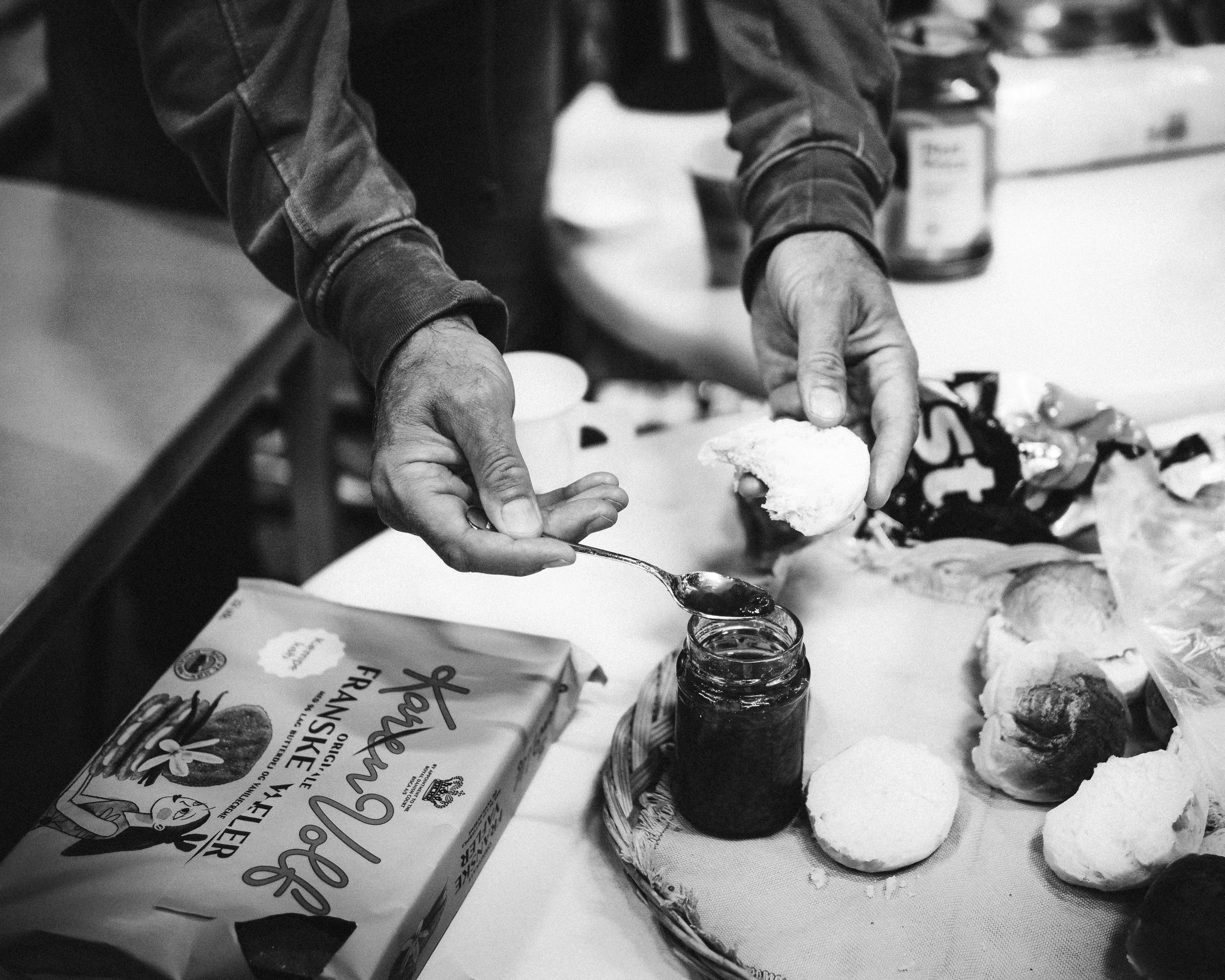 Close-up of hands preparing baked goods on a countertop, with various baking ingredients and baked bread rolls visible.