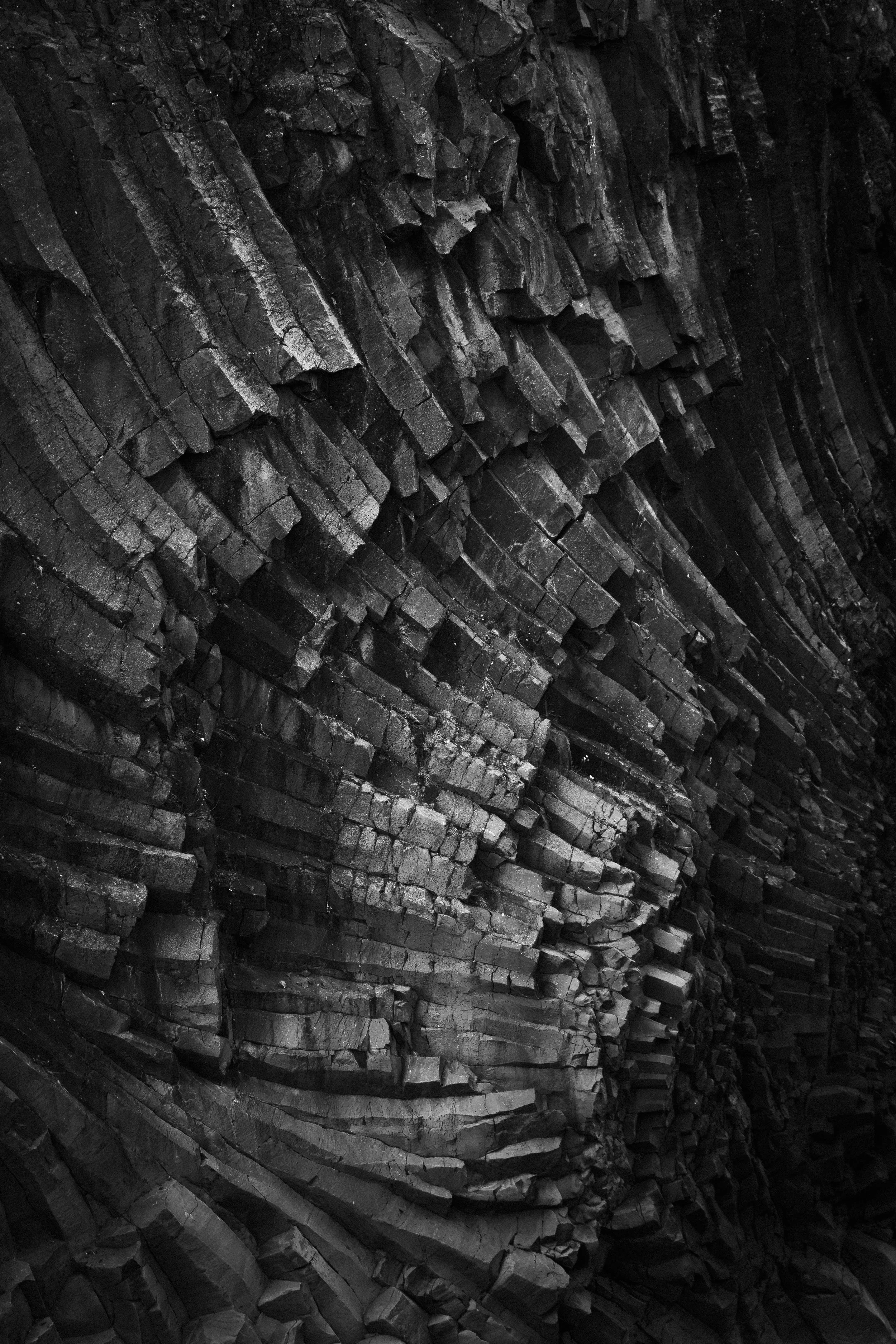 Close-up image of layered, dark gray/brown volcanic rock formations with a spiral or swirling pattern.