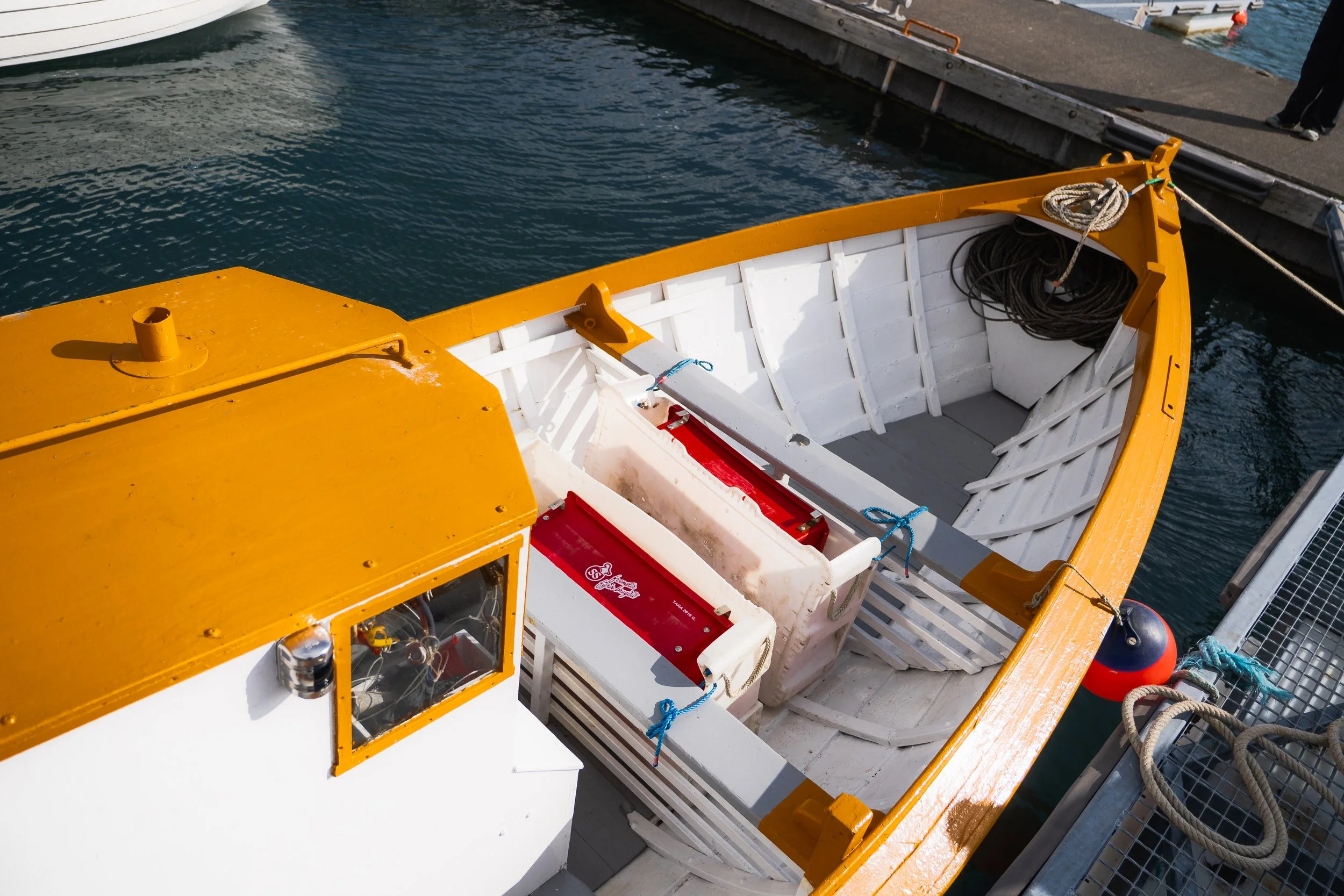 A boat docked at a pier with a yellow and white exterior, containing ropes and equipment, and another boat partially visible on the left side.