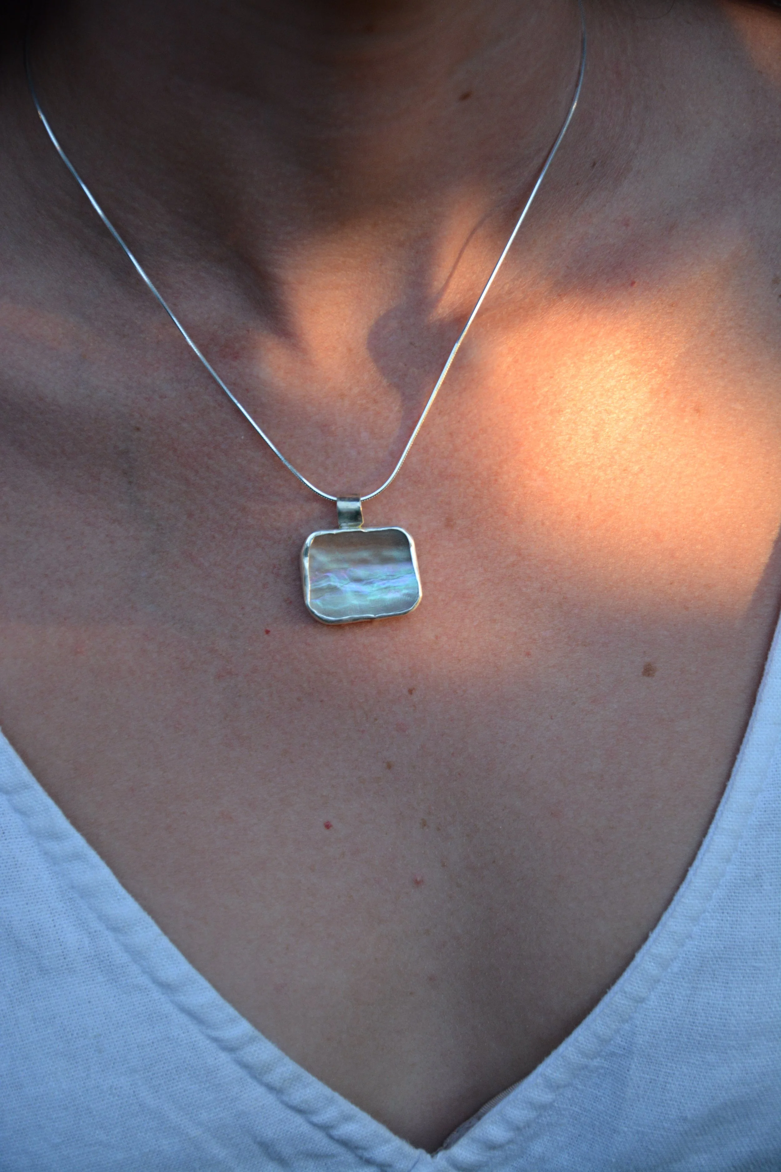 Close-up of a person's neck wearing a sterling silver necklace with a rectangular abalone pendant.