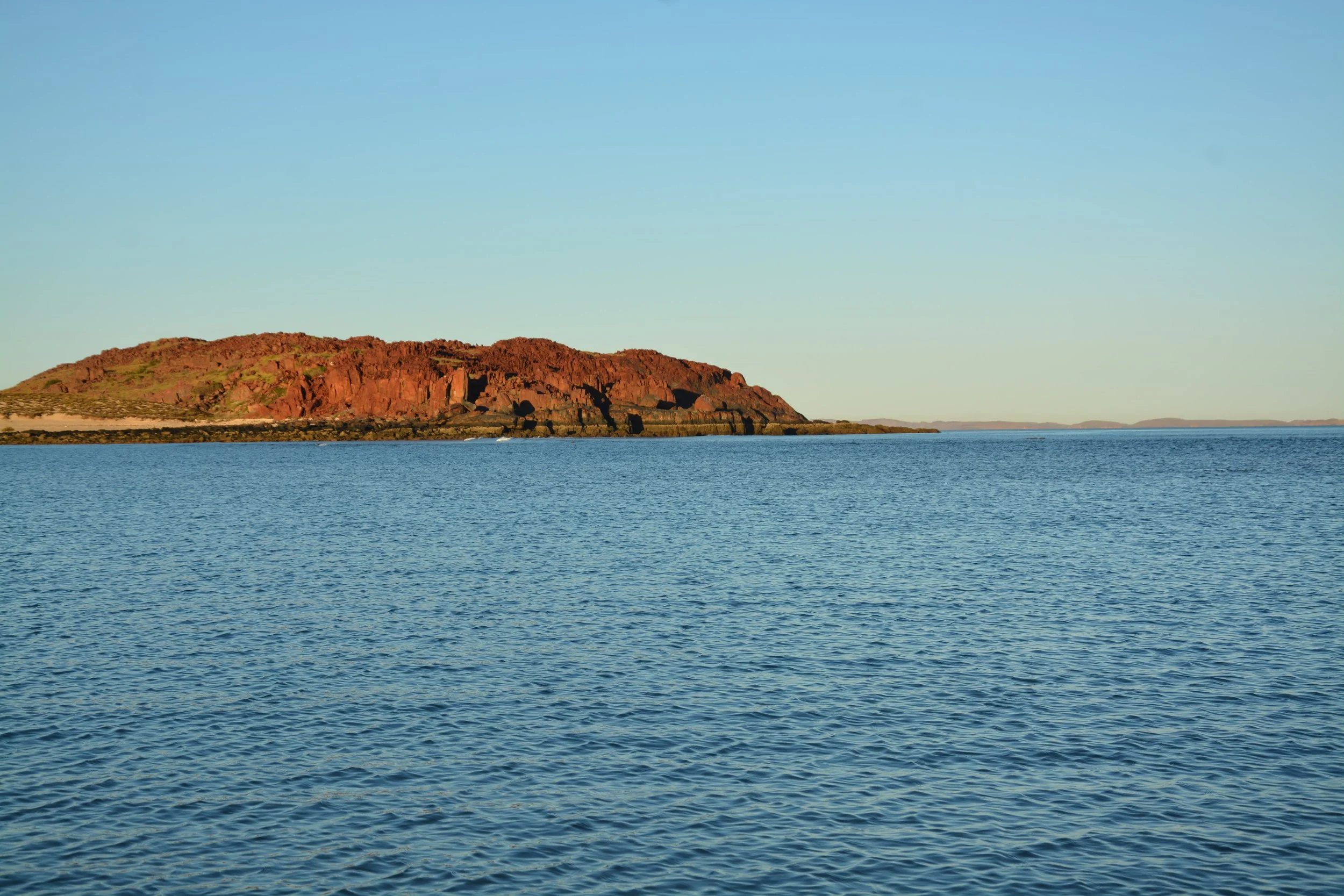 Ocean view with a rocky island in the distance under a clear blue sky.