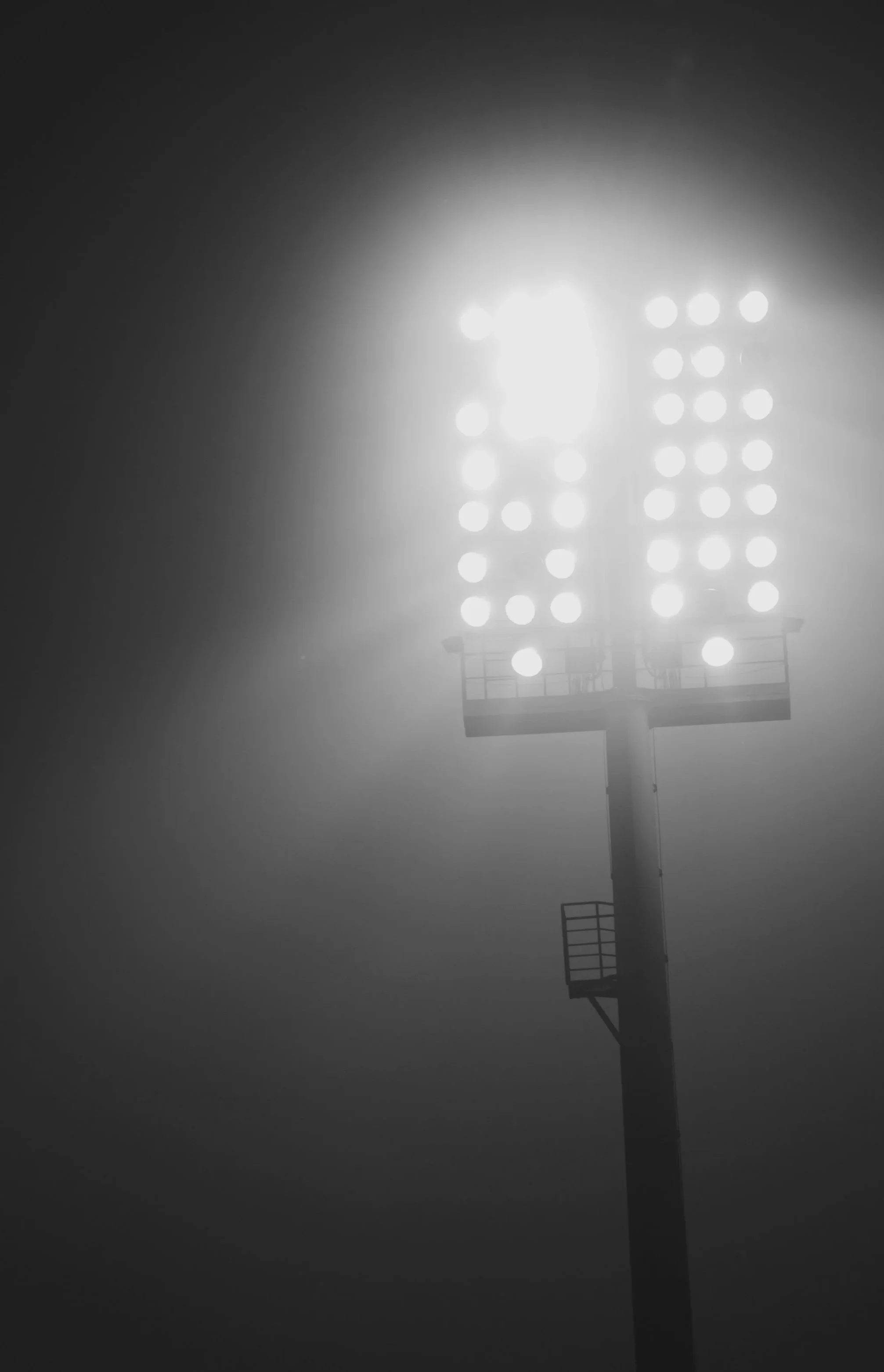A brightly lit floodlight tower on a foggy night, with the lights illuminating the mist around it.