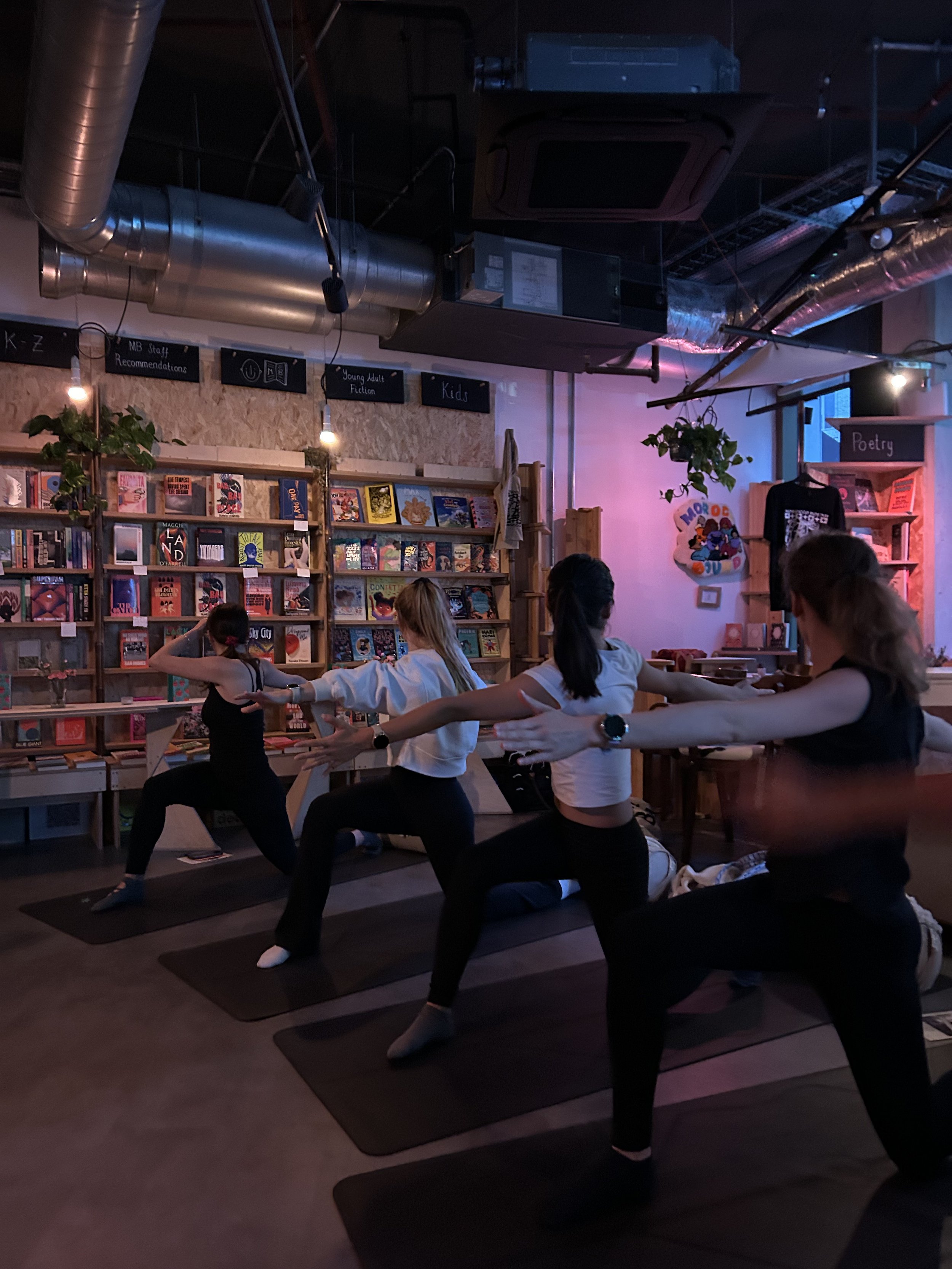 Group yoga class practicing in a bookstore surrounded by bookshelves and literary section signs