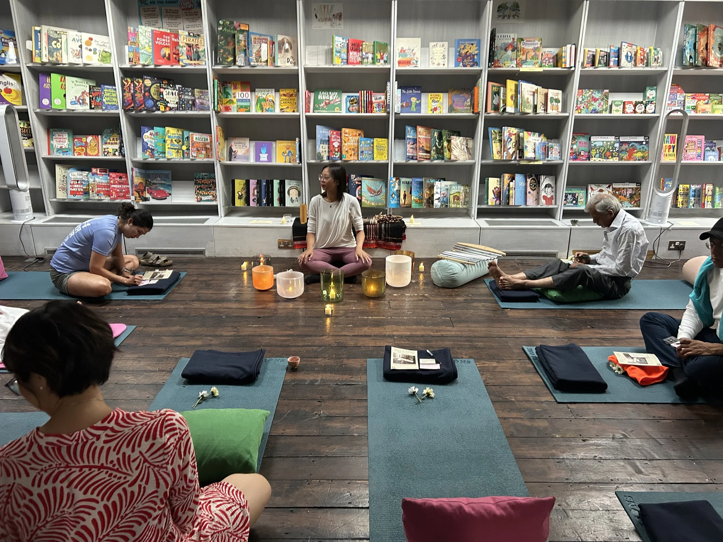 People meditating on yoga mats with candles in front of bookshelves filled with children's books.