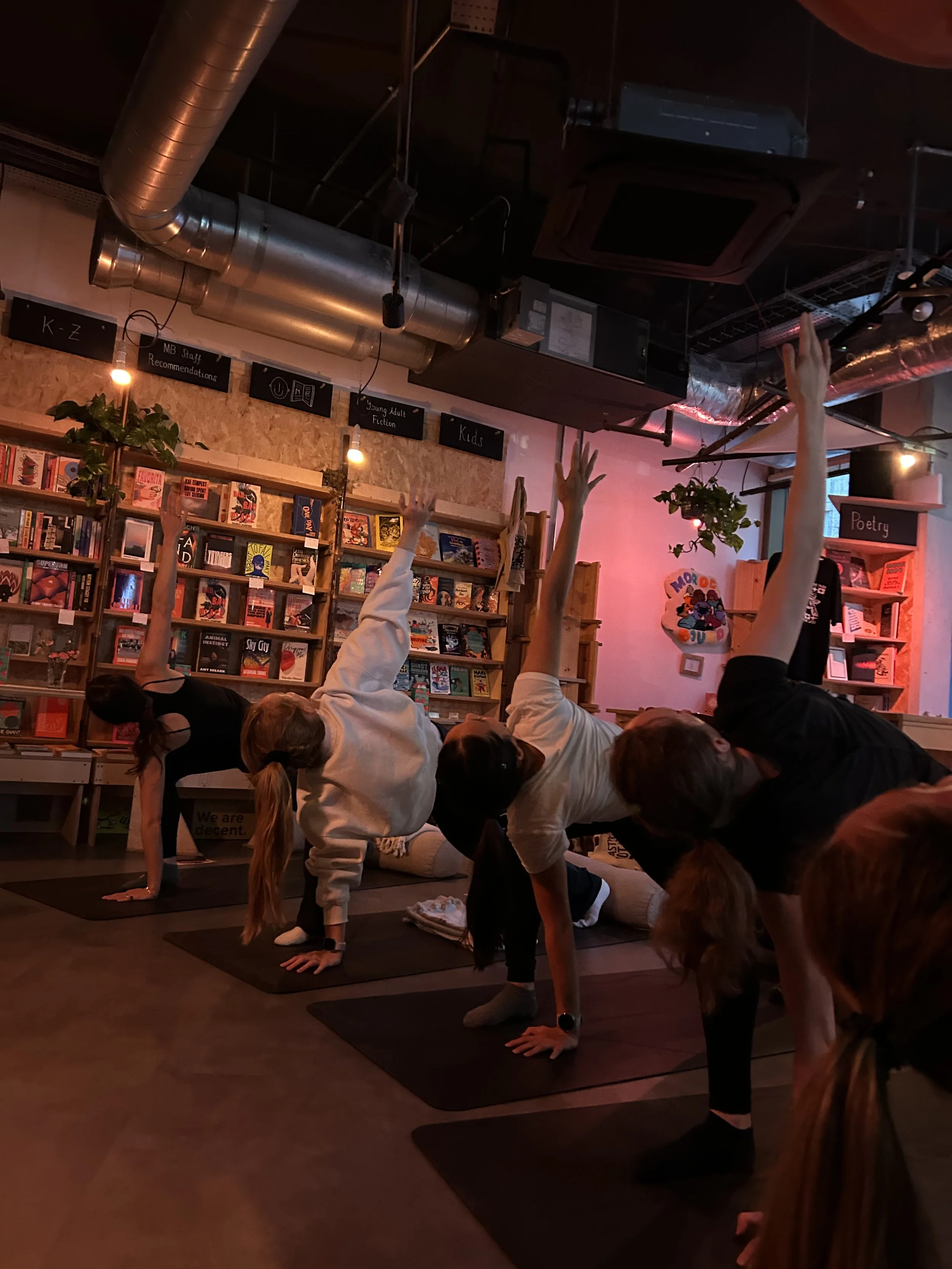 Group yoga class practicing downward-facing dog on mats inside a bookstore surrounded by bookshelves.