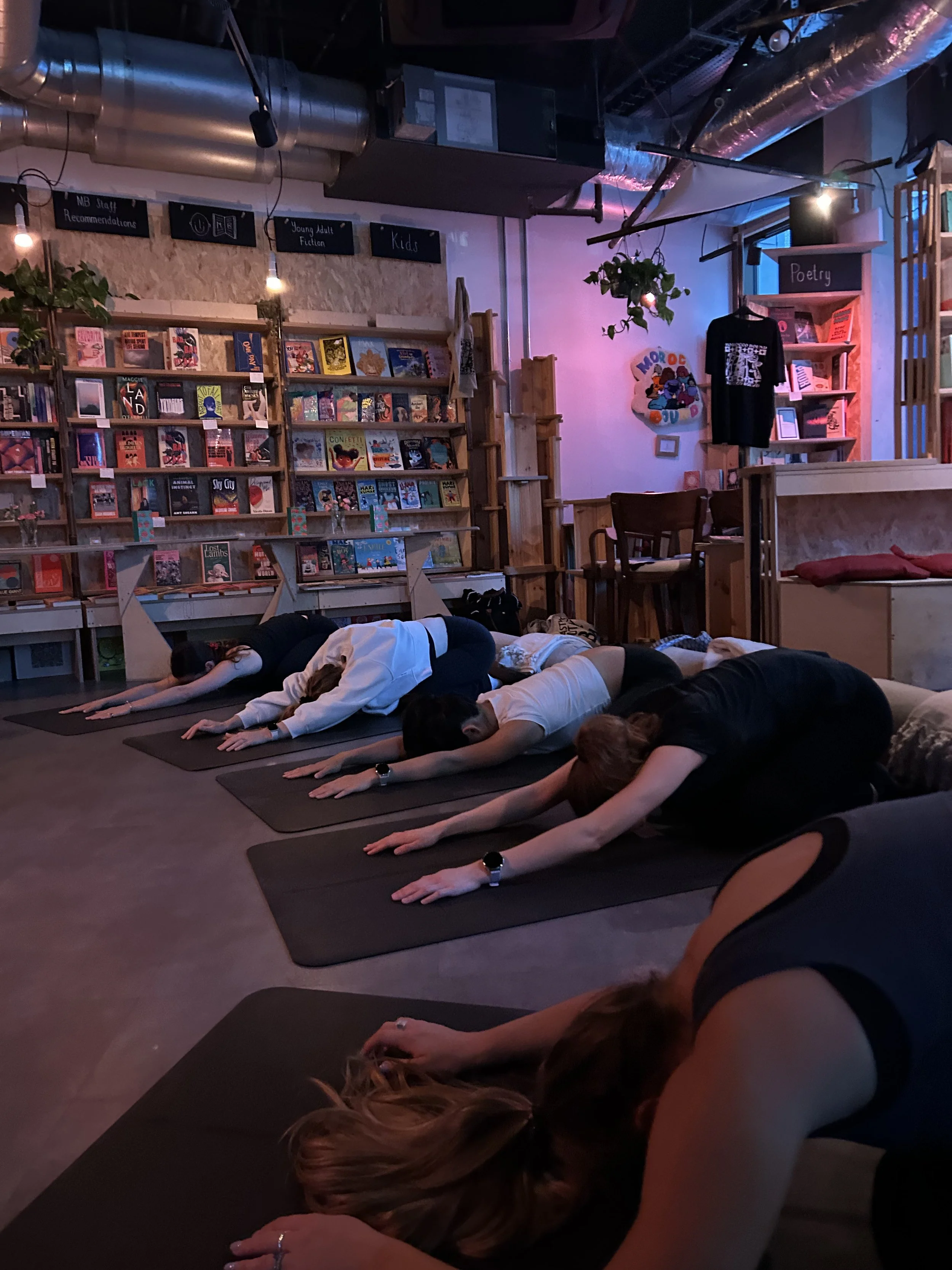 People practicing yoga on mats inside a colorful independent bookstore surrounded by bookshelves and literary signs
