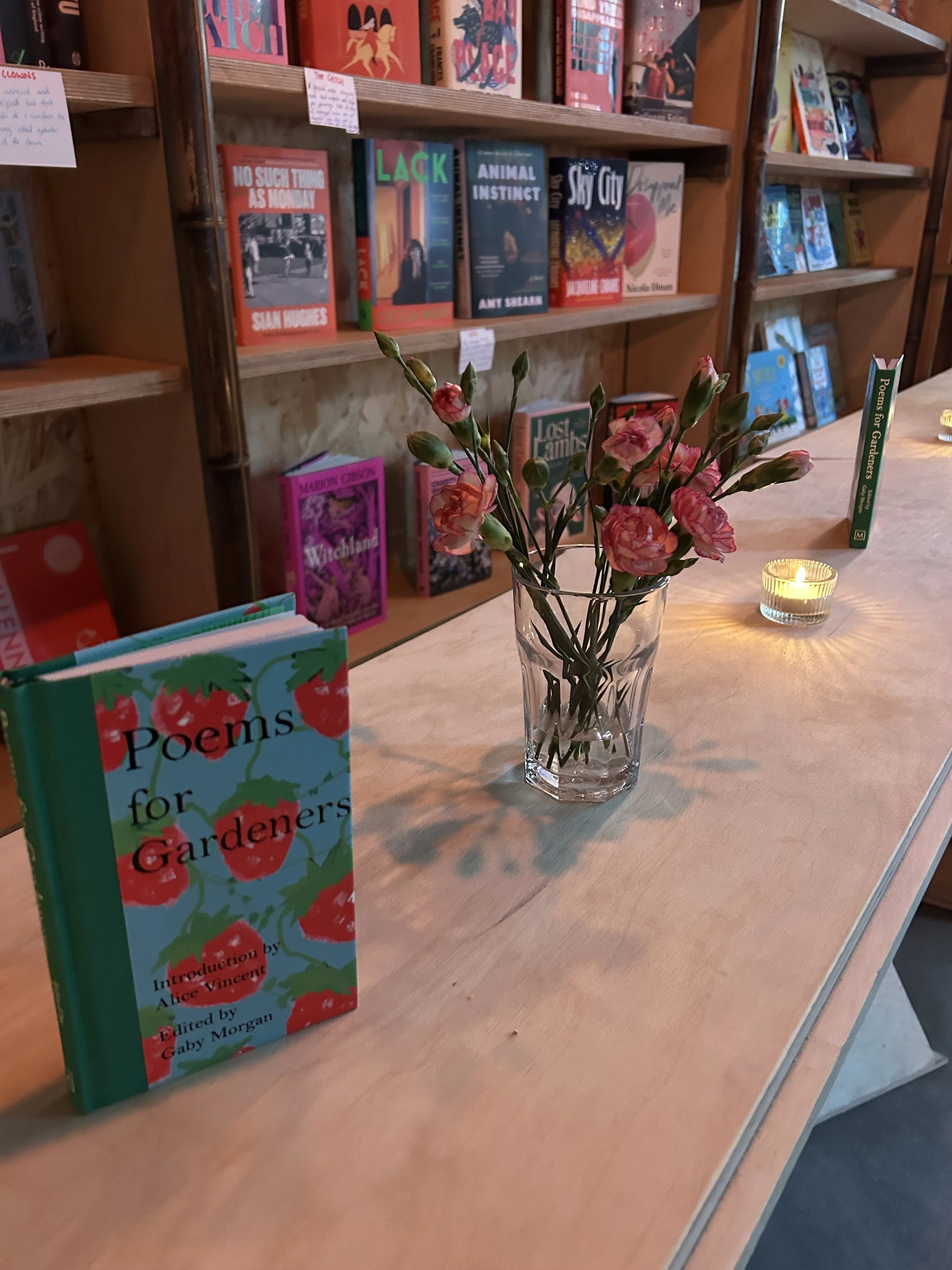 Bookshelves filled with books, a vase of pink flowers, and a lit candle on a wooden table.