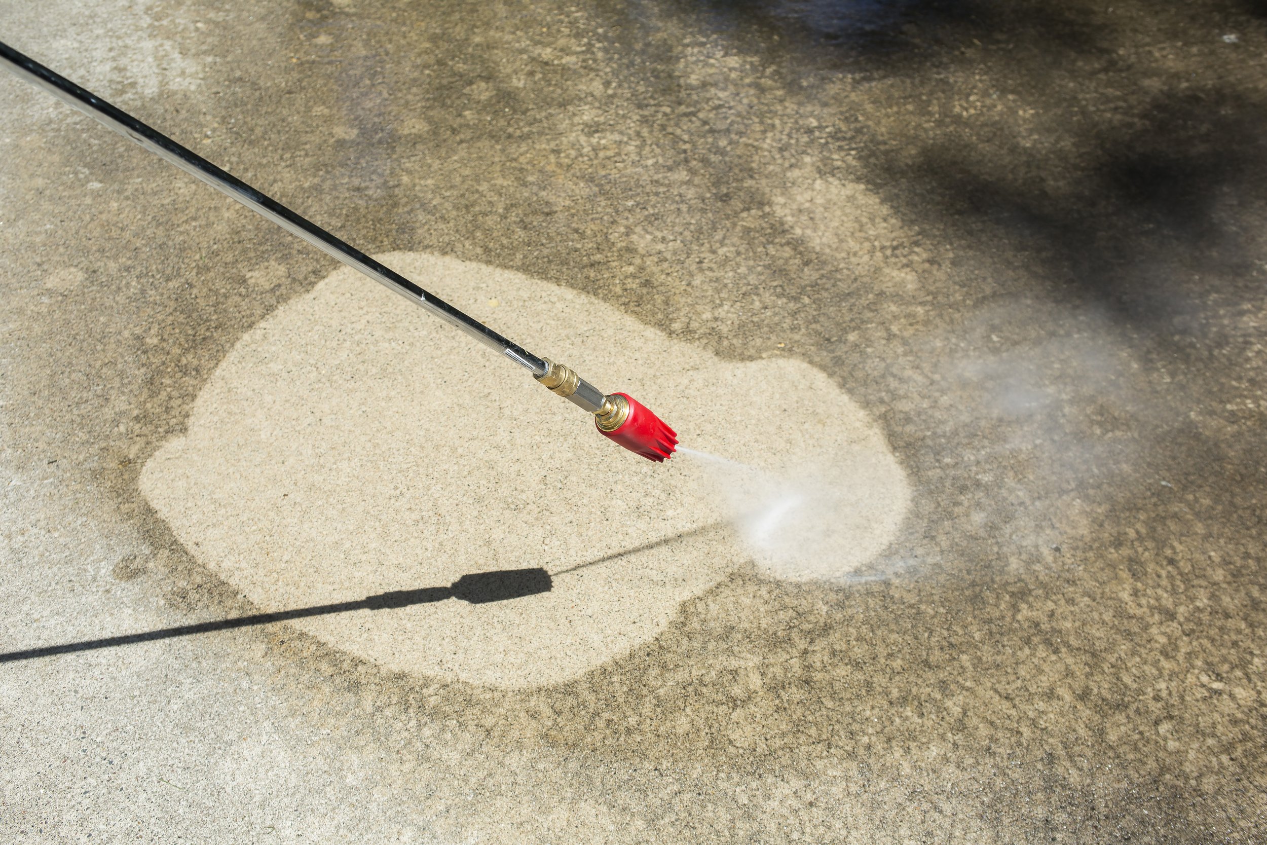 A pressure washer nozzle spraying water on sand, creating a clean outline of a shape on the ground.