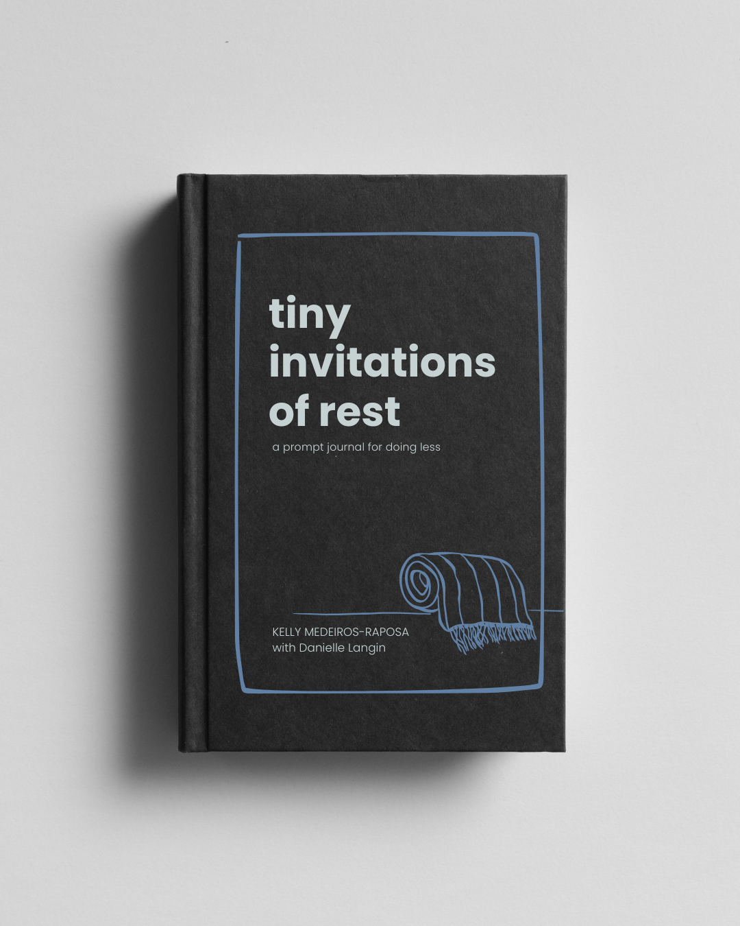 A black hardcover book titled 'tiny invitations of rest' with a subtitle 'a prompt journal for doing less', authored by Kelly Medeiros-Raposa with Danielle Langi featuring a simple line drawing of a rolled-up blanket or rug on the cover, placed against a light gray background.