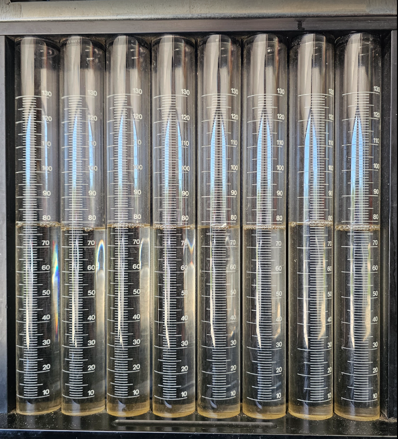 Close-up of multiple test tubes filled with liquid, labeled with measurement markings from 0 to 130 milliliters. Injectors have been tested and show a balanced system from flow testing.