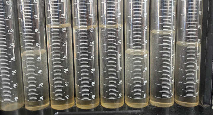 Clear graduated cylinders filled with a yellowish liquid, standing in a row on a lab shelf representing injector flow results from bad injectors.