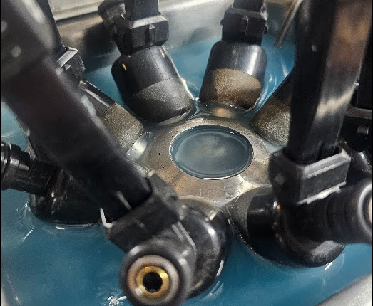 Close-up of injectors being cleaned in an ASNU cleaning solution getting pulsed while ultrasonic cleaned.