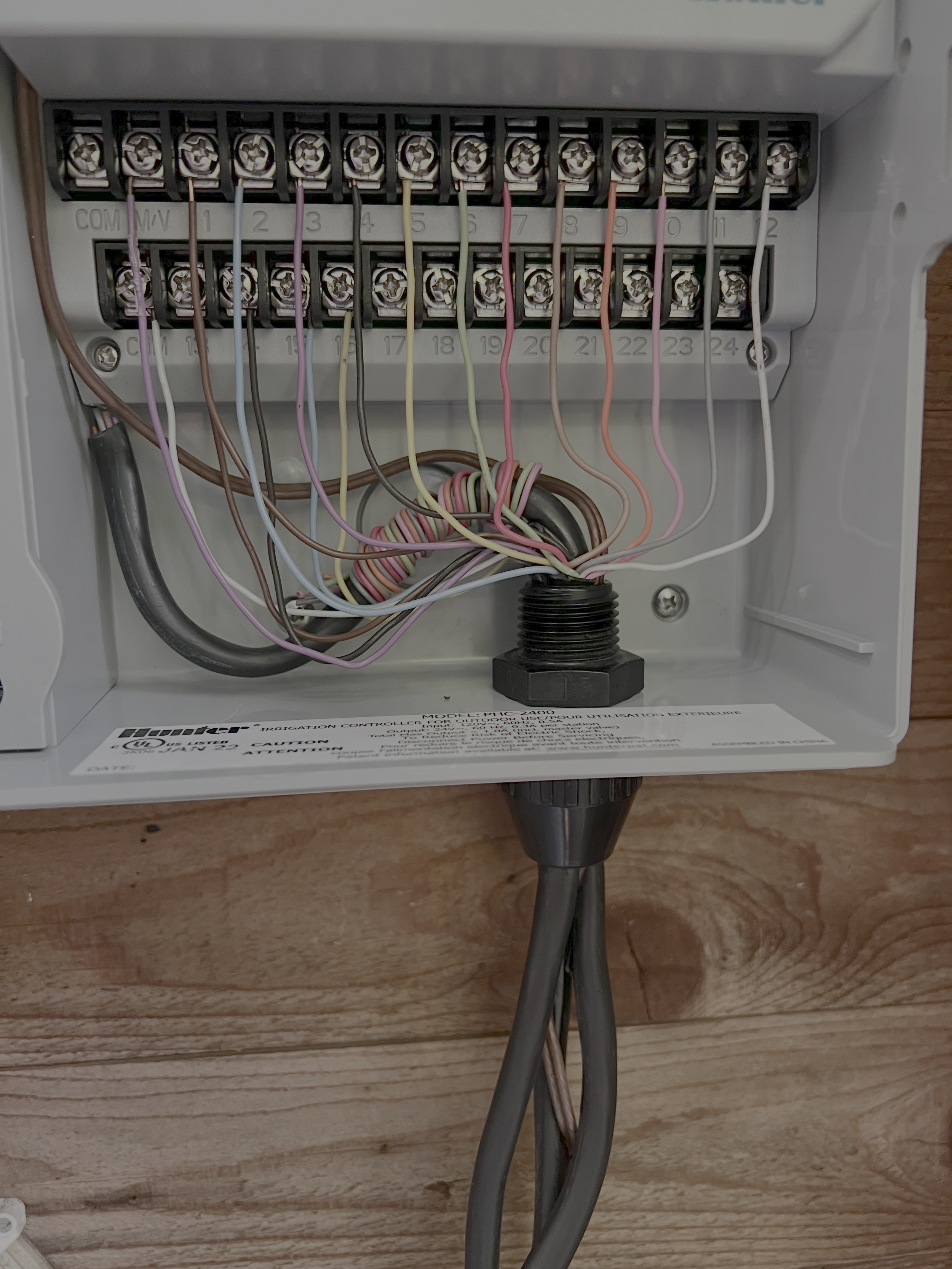 Electric irrigation controller with multiple wires connected inside a white plastic box.