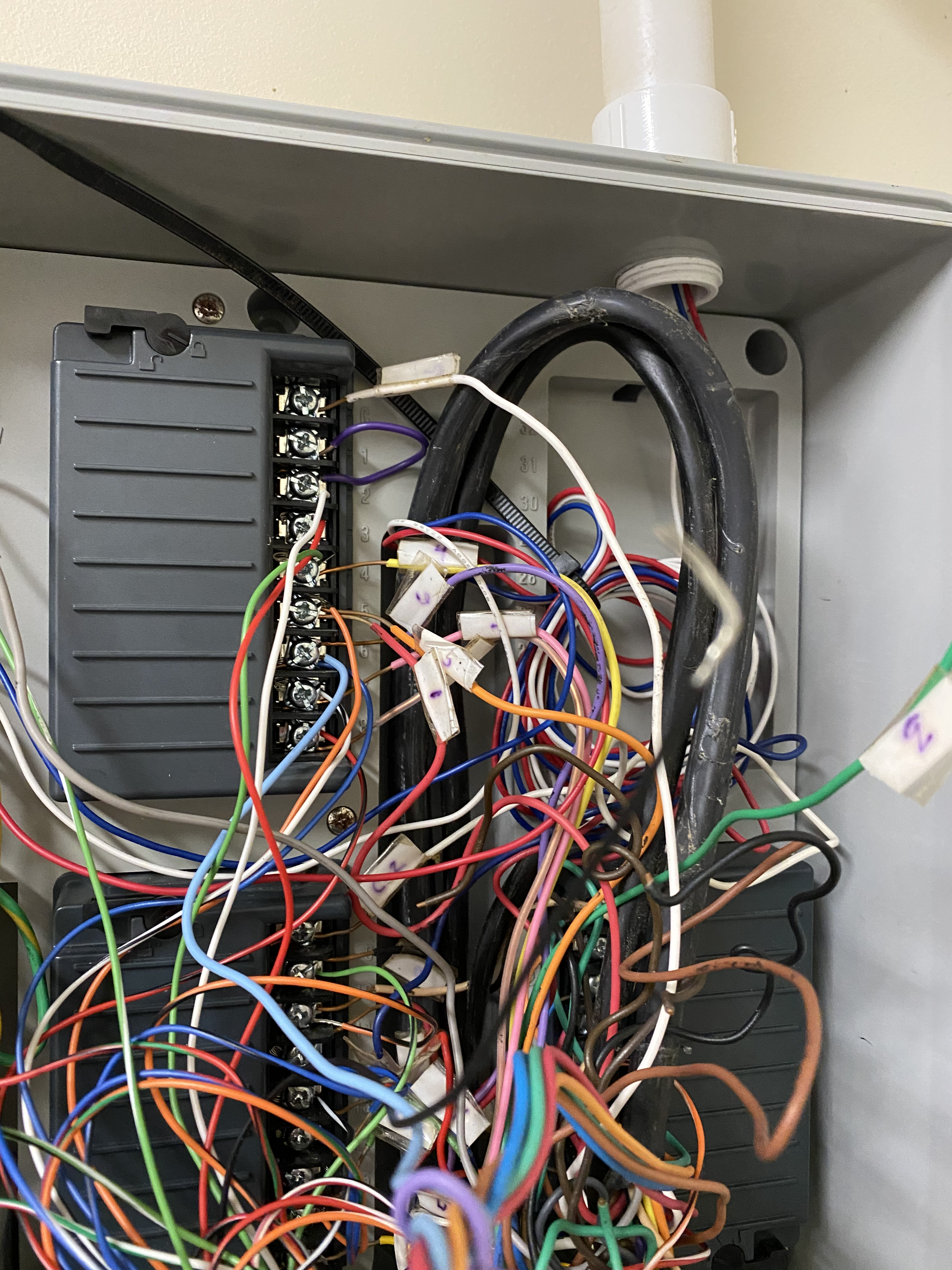 Inside of an electrical panel with multicolored wires, a gray component on the left, and a black cable.