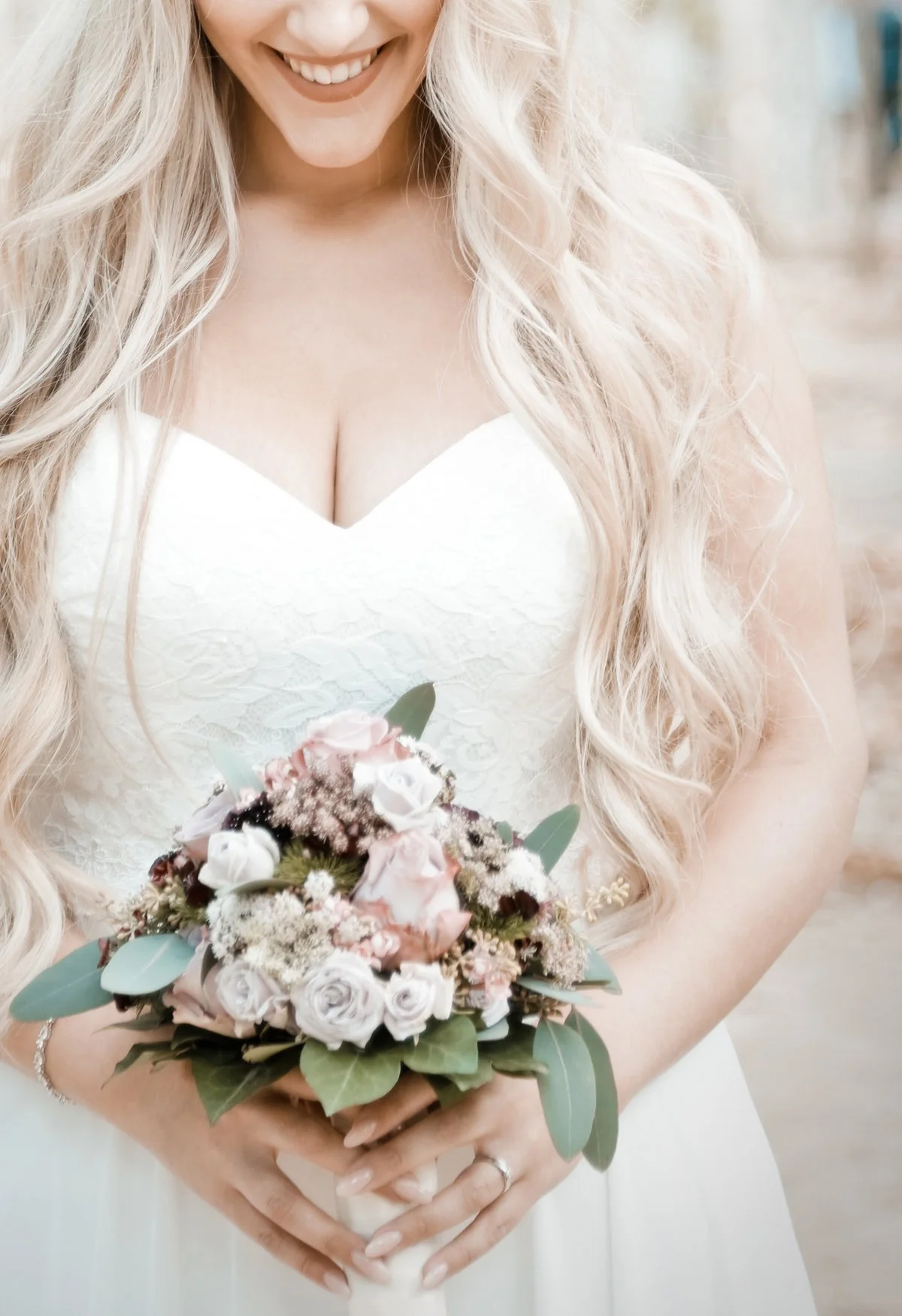 Frau in weißem Brautkleid hält einen Blumenstrauß mit weißen und rosa Blumen und grünen Blättern.