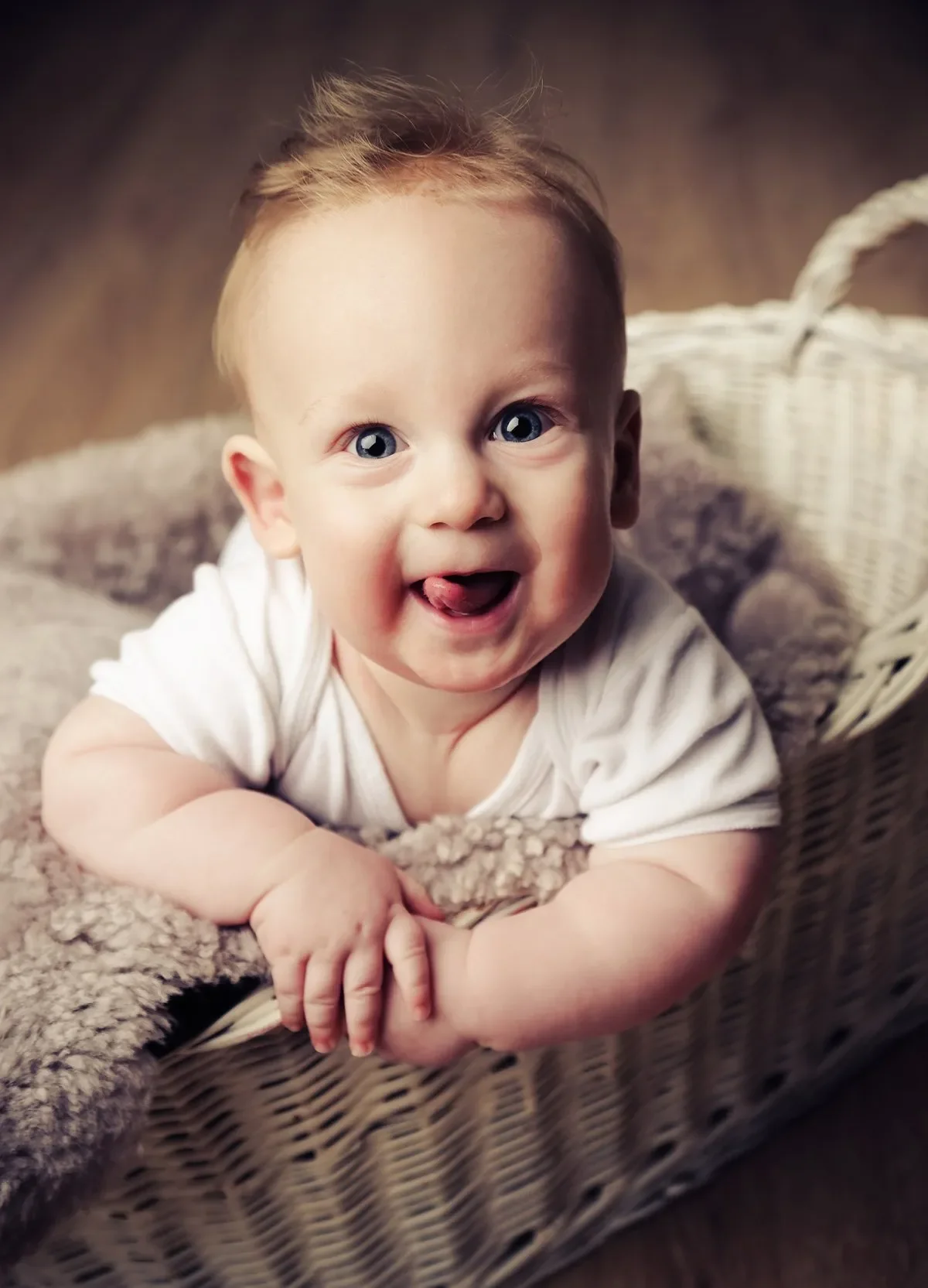Baby Fotoshooting im Fotostudio - Ein lachendes Baby mit blonden Haaren liegt auf einer weichen Decke in einem Korb.