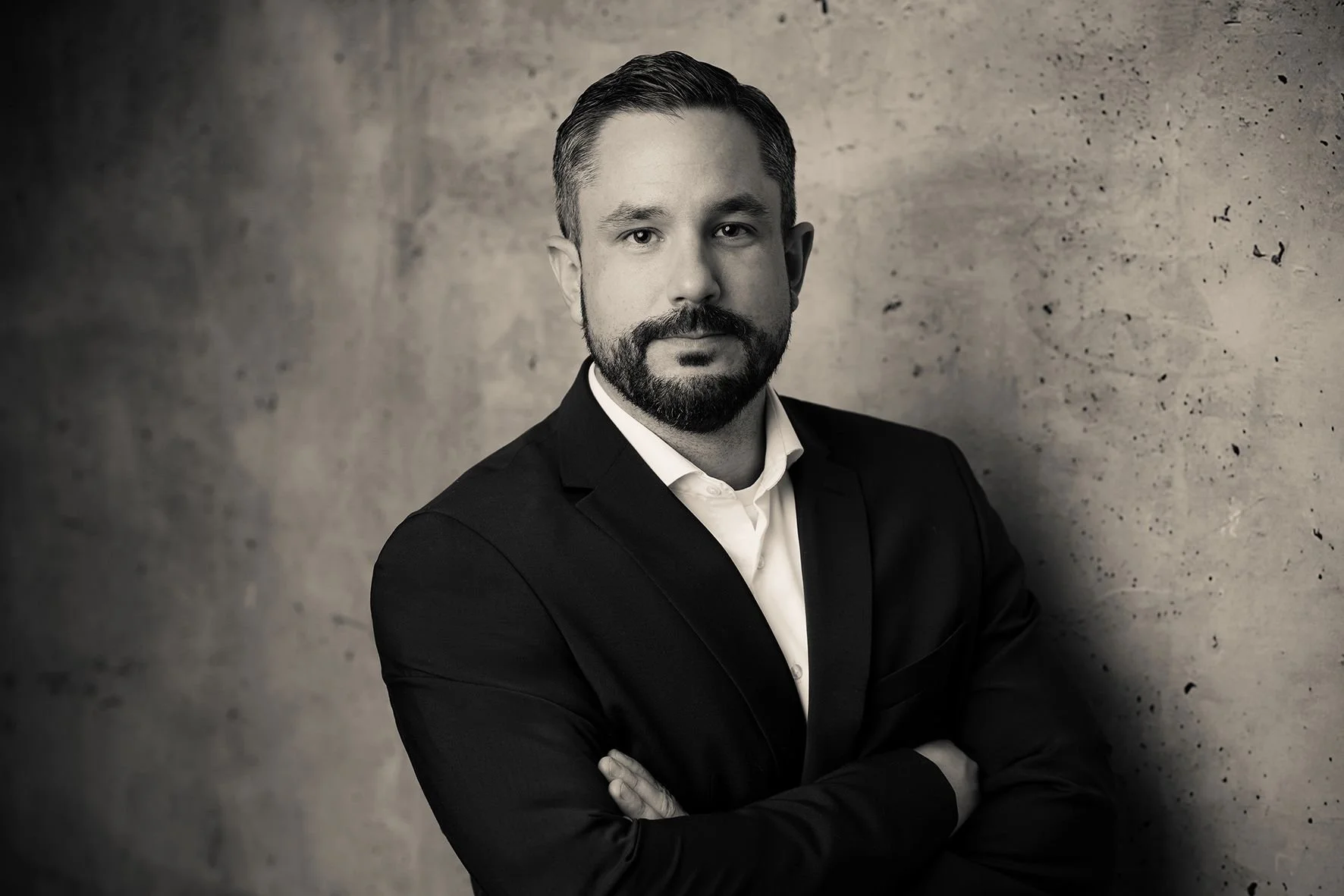 Bewerbungsfoto in moderenem Fotostudio - Schwarz-weißer Portrait eines manns in Anzug mit verschränkten Armen vor einer Betonwand.