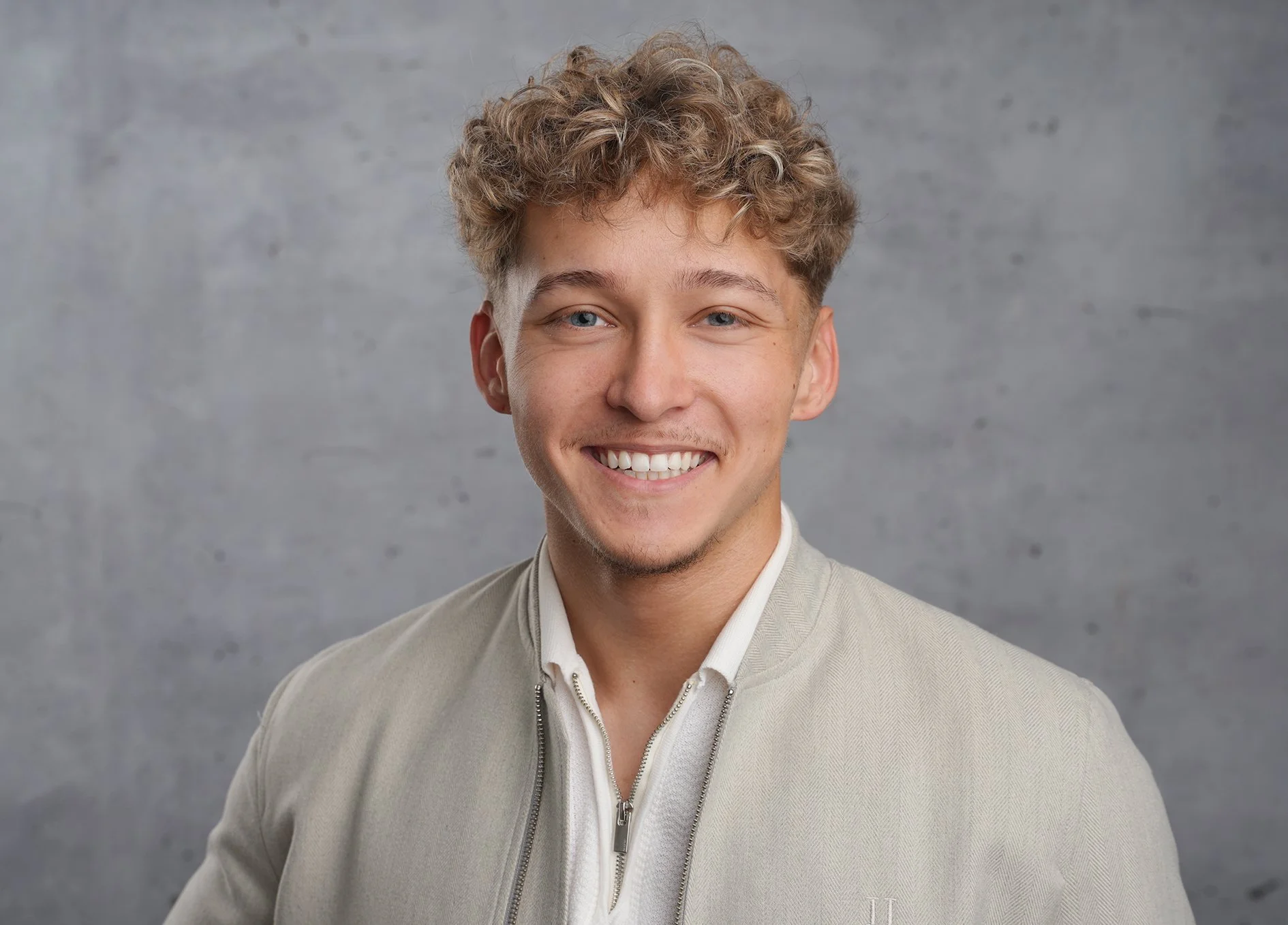 Modernes Bewerbungsfoto im Fotostudio in Darmstadt - Junge Mann mit lockigem Haar und lächelnd, vor grauem Hintergrund.