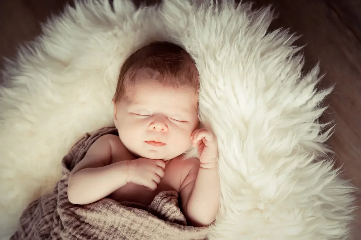 Fotoshooting im Fotostudio in Darmstadt - Neugeborenes Baby schläft auf einem flauschigen, weißen Tuch, eingewickelt in eine braune Decke.