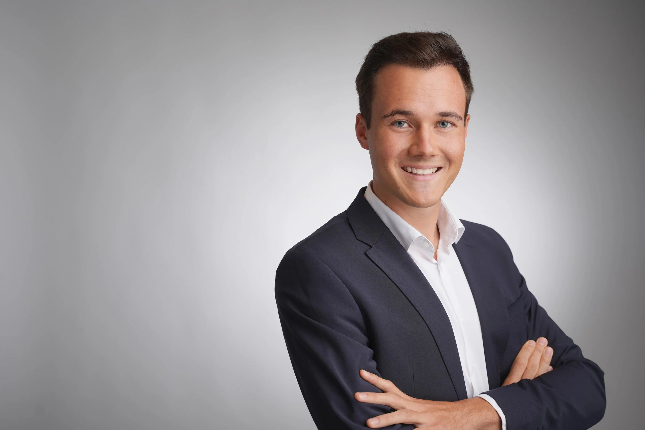Modernes Bewerbungsfoto im Fotostudio in Darmstadt - Junger Mann in dunklem Anzug mit weißem Hemd, lächelnd vor grauem Hintergrund.