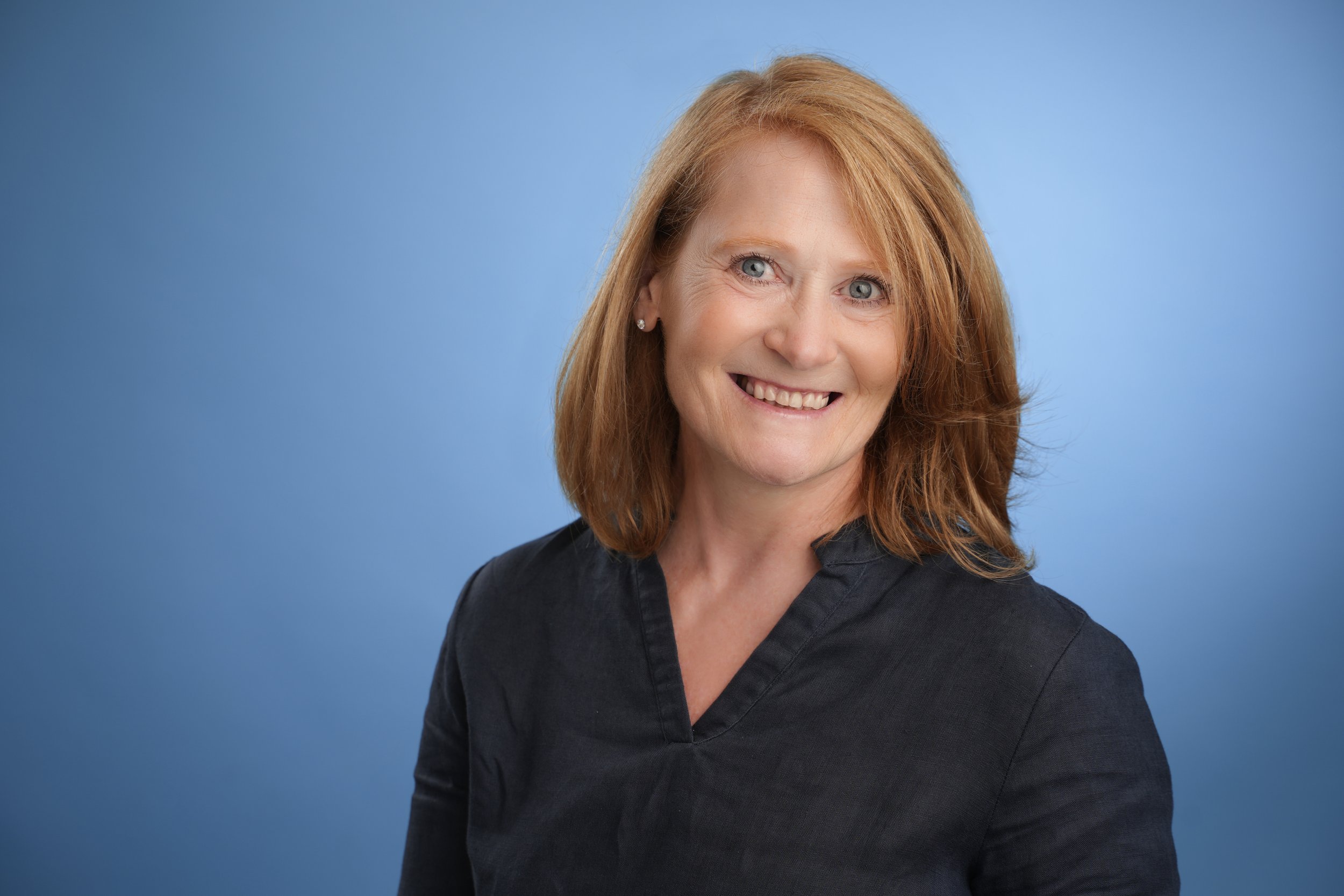Modernes Bewerbungsfoto im Fotostudio in Darmstadt - Lächelnde Frau mit rotbraunen Haaren und blauen Augen vor blauem Hintergrund