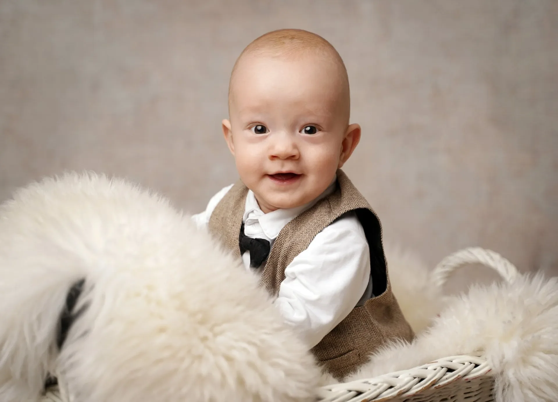 Babyfotoshooting - Süßer Baby mit blonden Haaren und braunem Anzug sitzt in einem Korb zwischen weißen, plüschigen Enten.