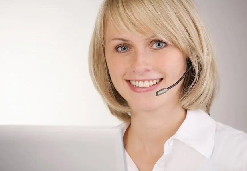 Frau mit blondem Haar trägt ein Headset und arbeitet an einem Computer.