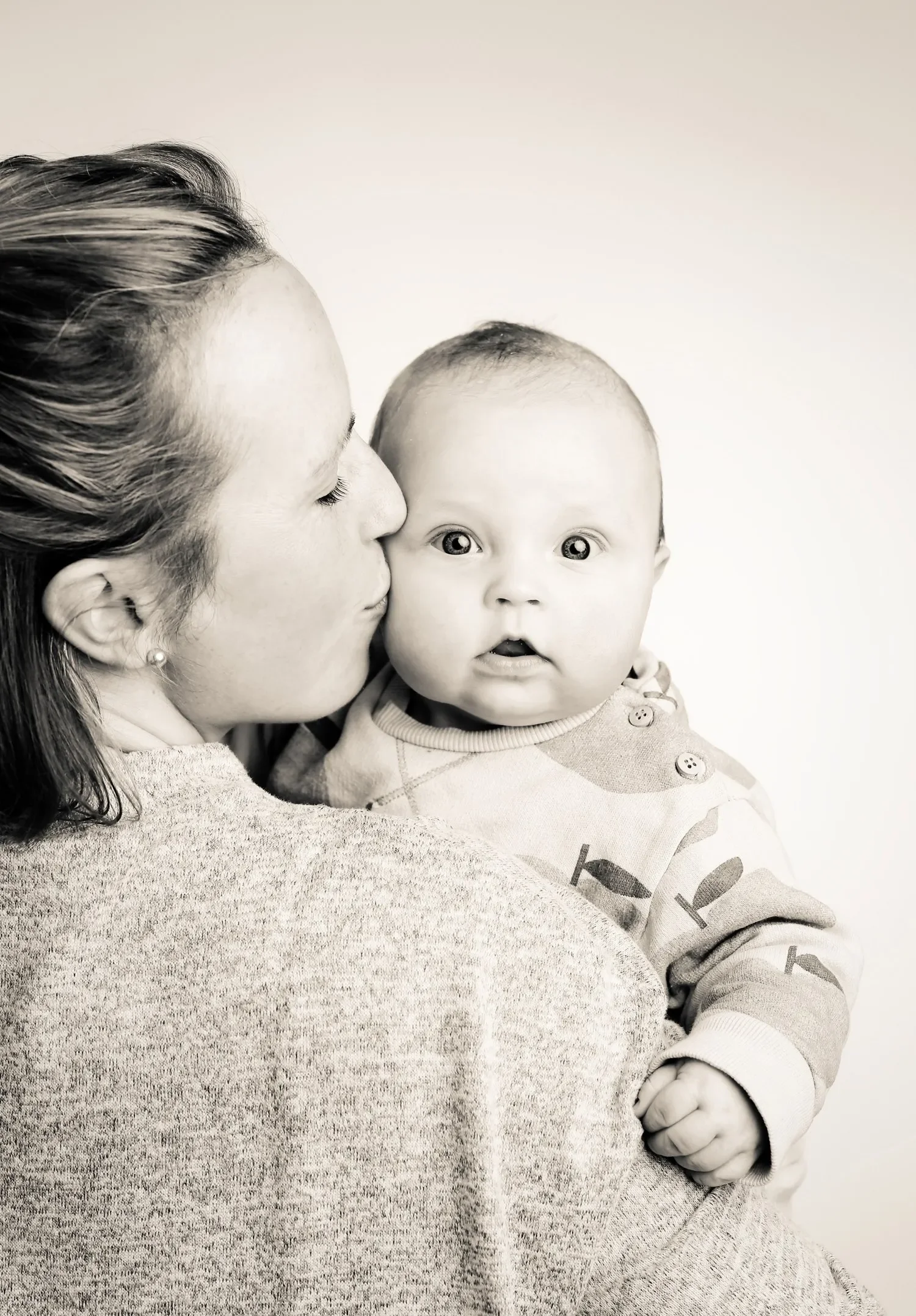 Eine Frau küsst ein Baby auf die Wange, beide schauen in die Kamera. Schwarz-Weiß-Foto, Nahaufnahme.