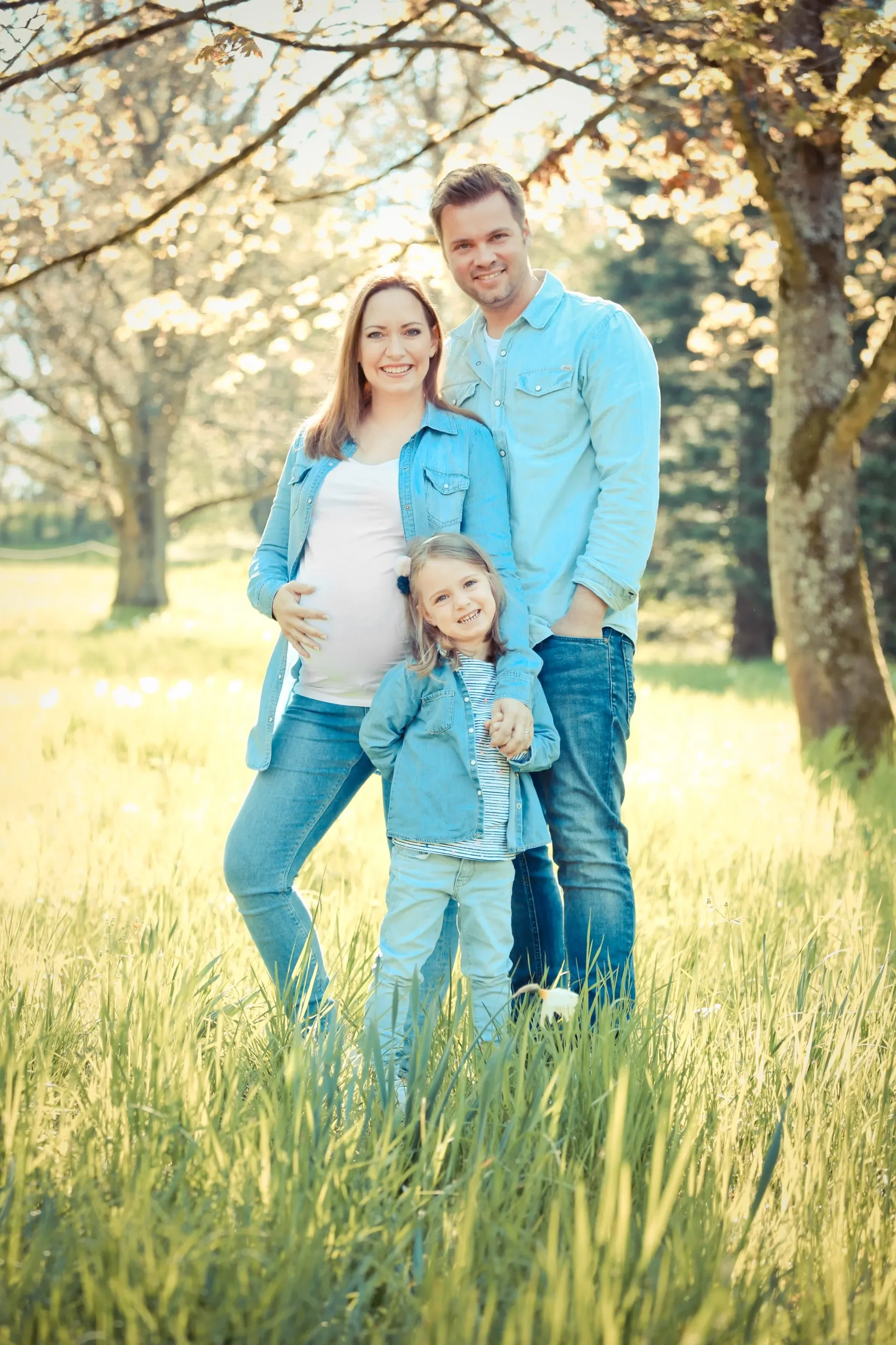 Familienfotoshooting im Park, Outdoor. Familie mit Mutter, Vater und zwei Kindern steht im Park im Sonnenschein.