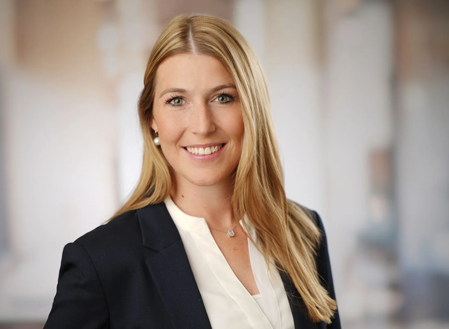 Business Bild - Porträt einer lächelnden Frau in Geschäftskleidung mit blondem Haar vor einem unscharfen neutralen Hintergrund. Bewerbungsfoto in modernem Fotostudio in Darmstadt aufgenommen.