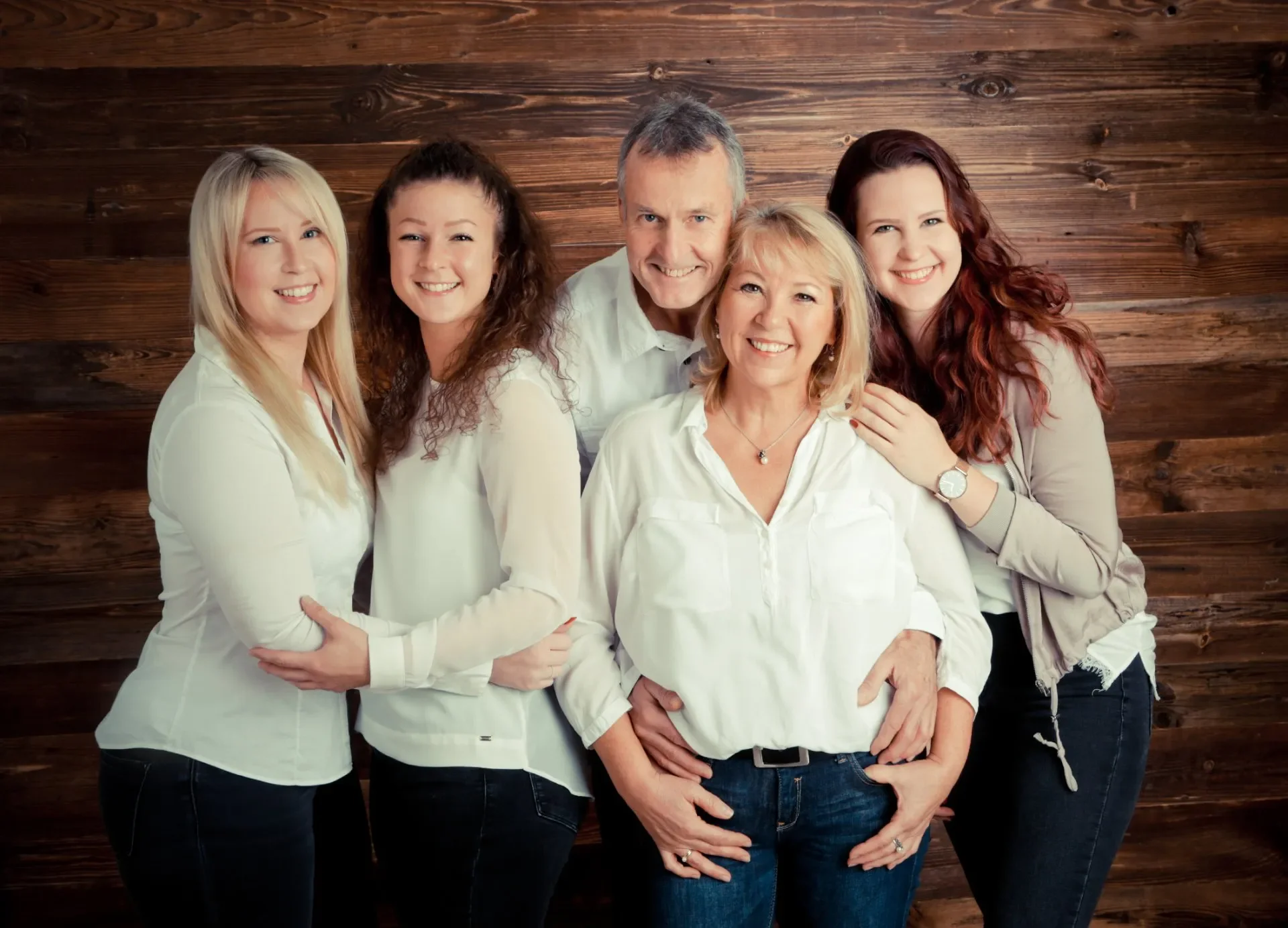 Familien Portrait Eine Gruppe von fünf Erwachsenen, die vor einer Holzwand steht, alle lächeln und tragen helle Oberteile.