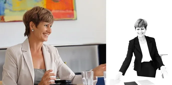 Ein Lächeln einer Frau in einem hellen Business-Outfit, im Büro, neben einem schwarzen und weißen Bild einer anderen Frau in formeller Kleidung