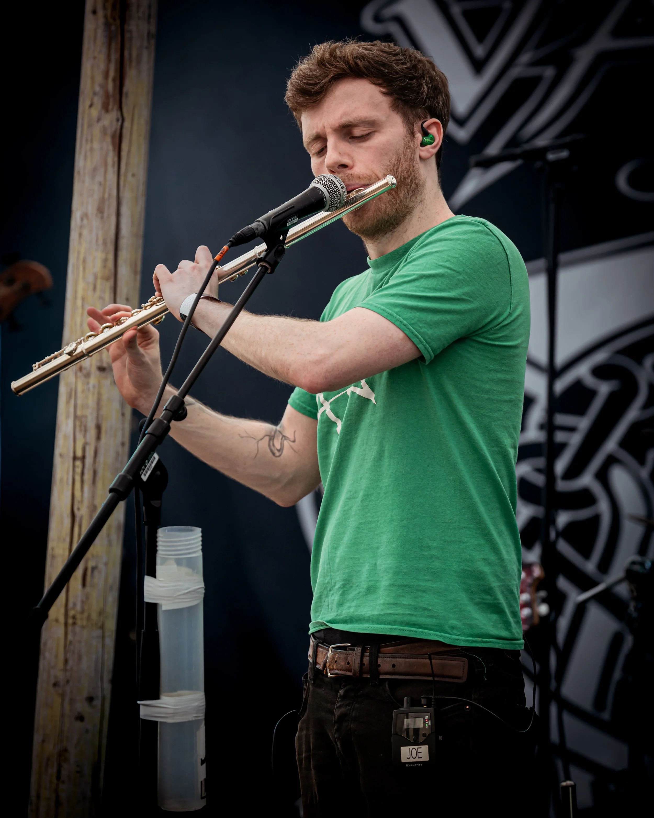 A man in a green t-shirt playing the flute at an outdoor event.