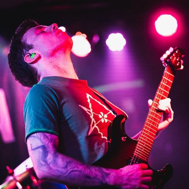 Musician playing electric guitar on stage with colorful stage lights.