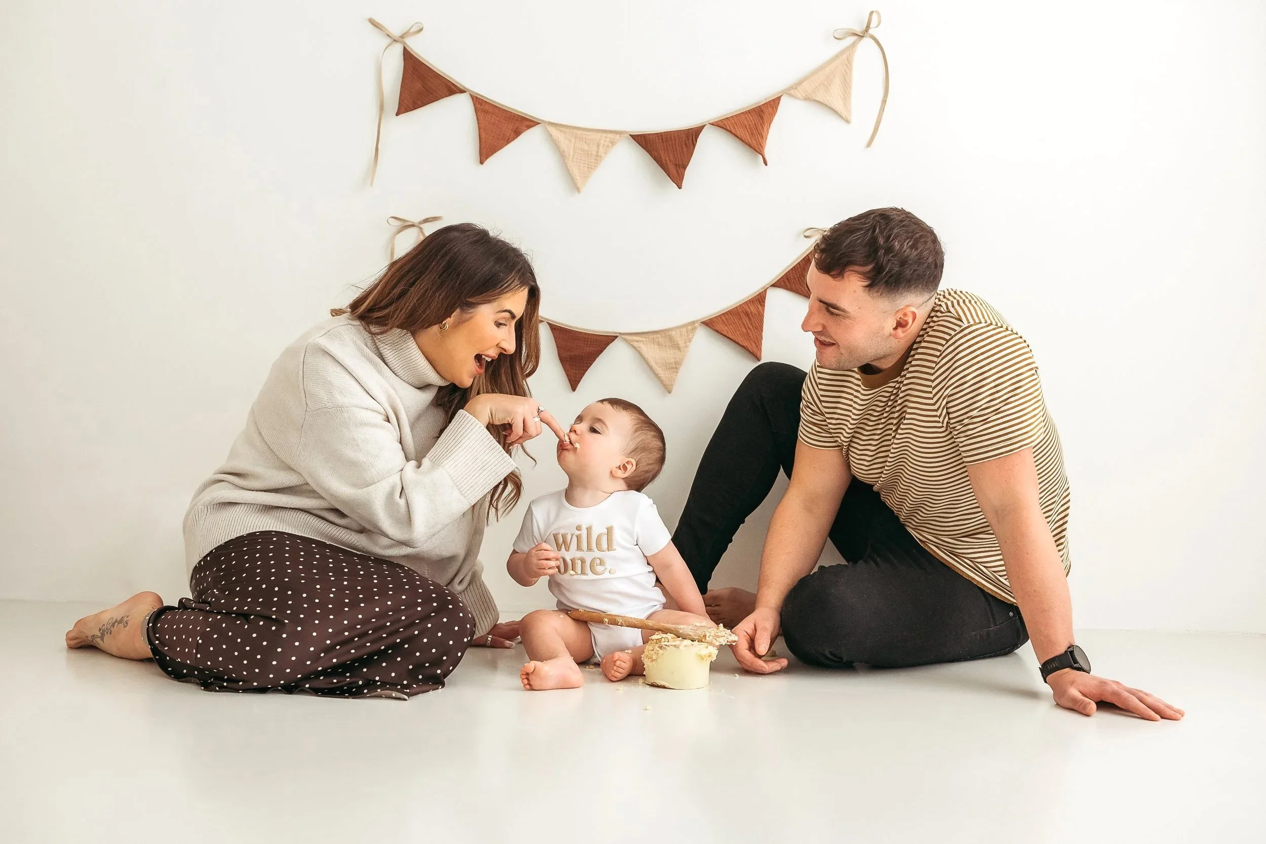 Family celebrating their baby’s first birthday with a cake during a studio photography session.