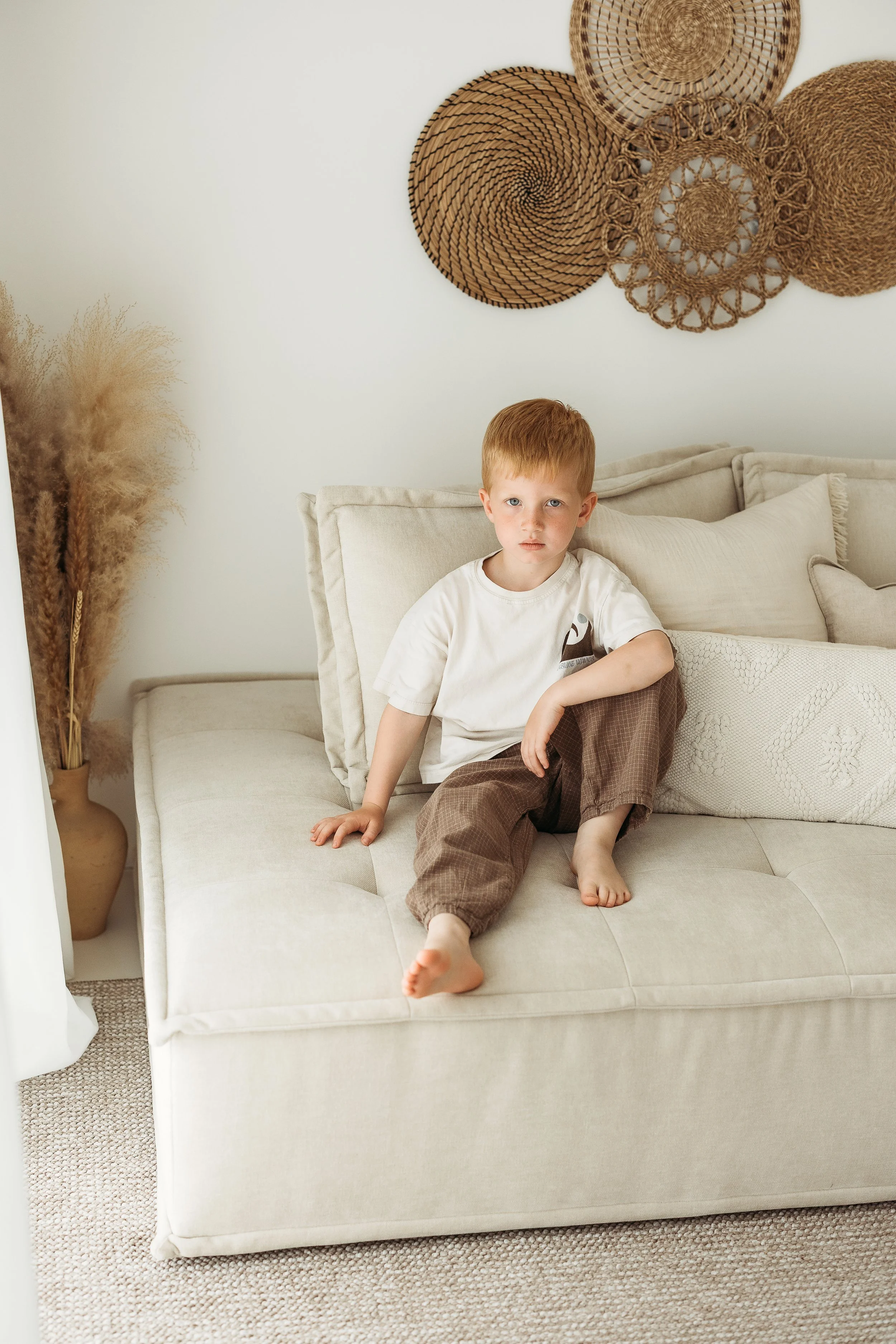 Young boy sitting and smiling on a cream sofa during a relaxed studio portrait session.