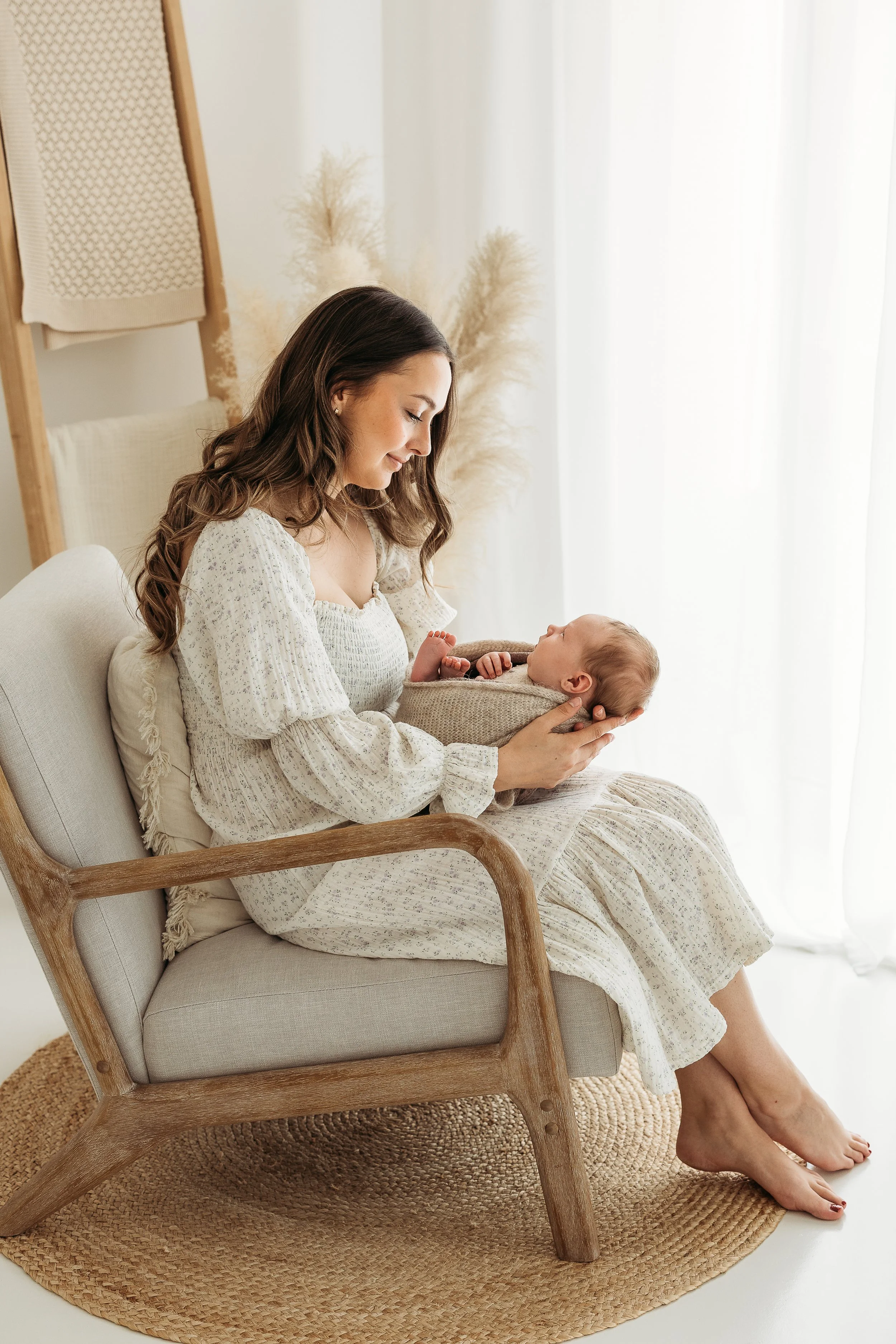 Mum sitting by the window and cuddling her newborn baby during a relaxed studio newborn session.