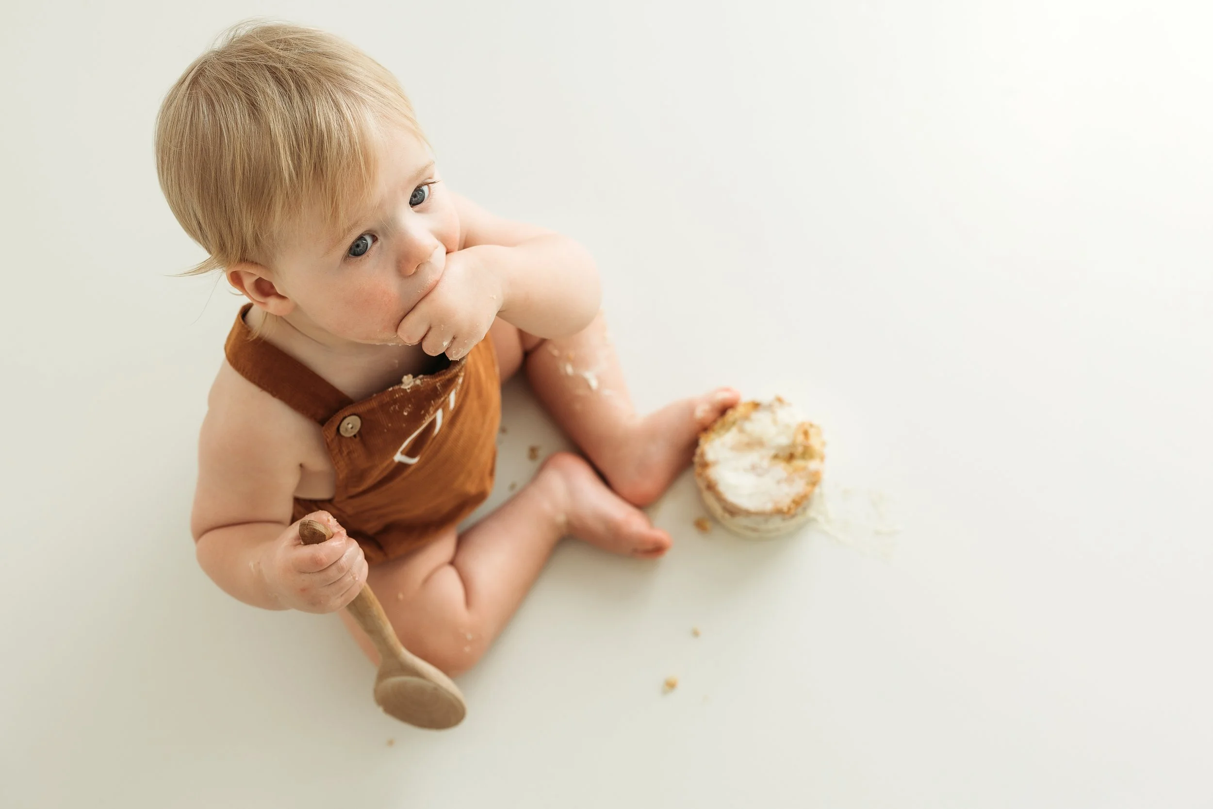Toddler enjoying cake with messy hands and crumbs during a fun first birthday cake smash session