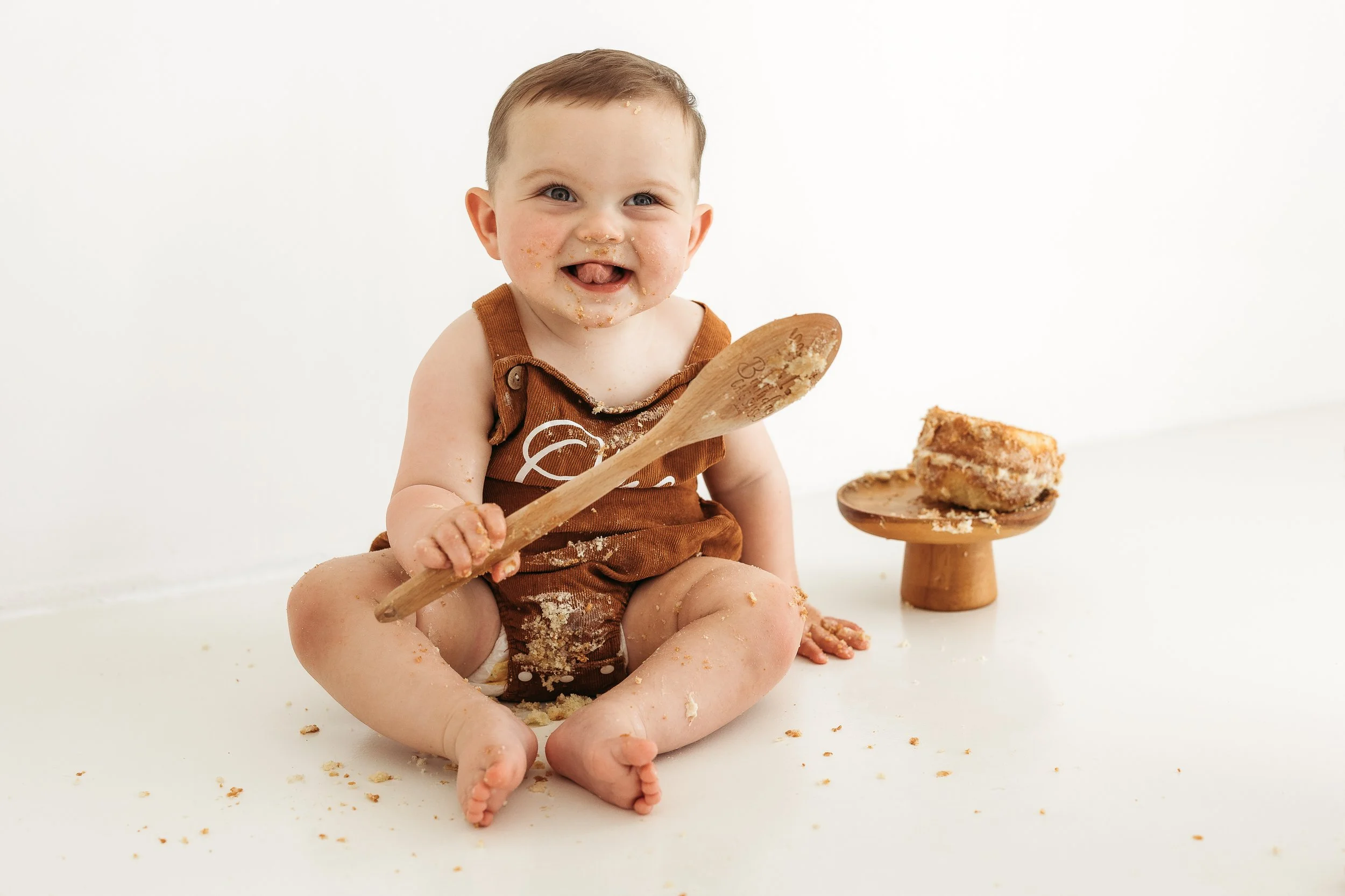Toddler enjoying cake with messy hands and face during a fun first birthday photography session