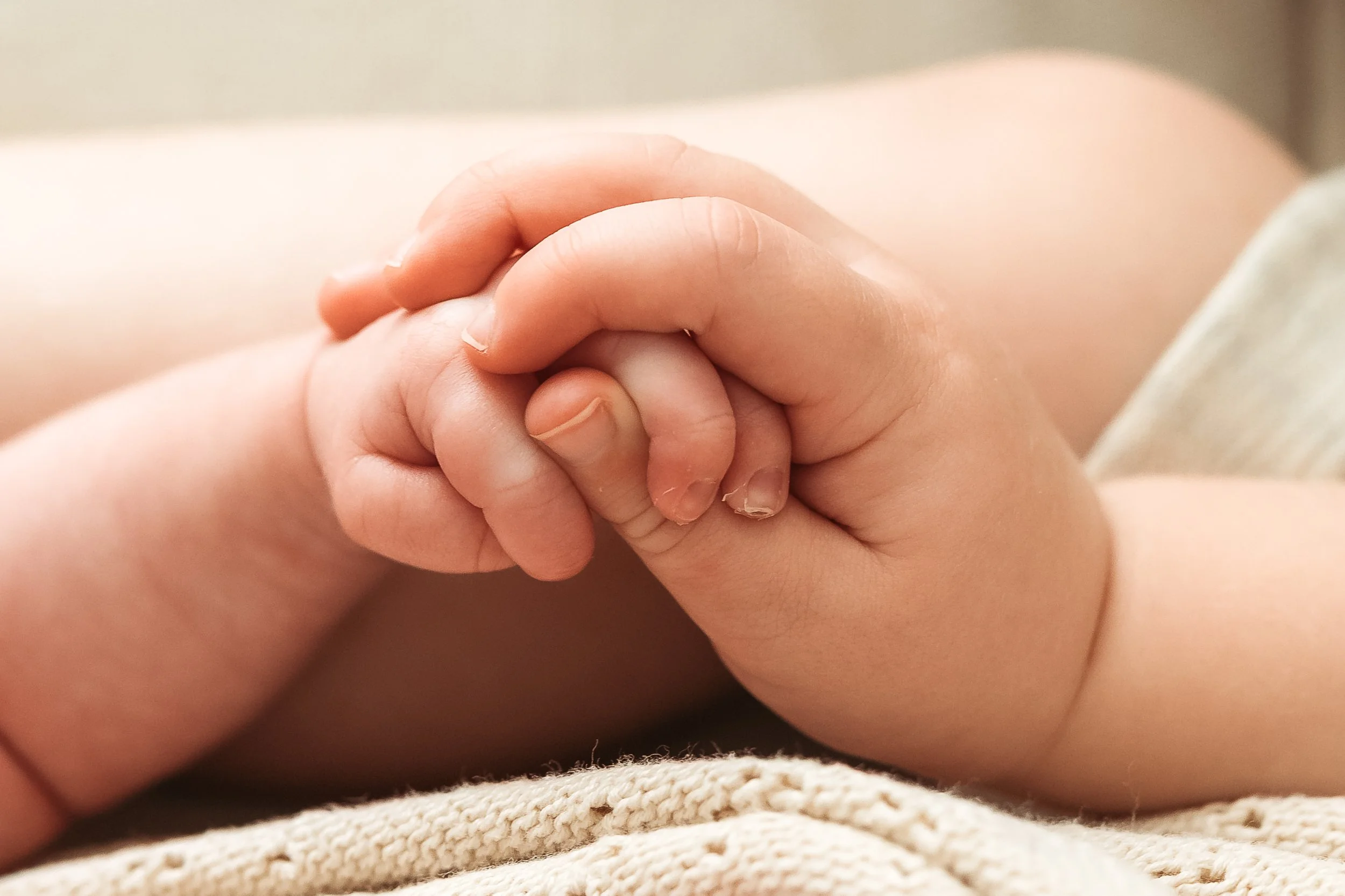 Close-up of a small child's hand holding an adult's finger in a gentle grip.