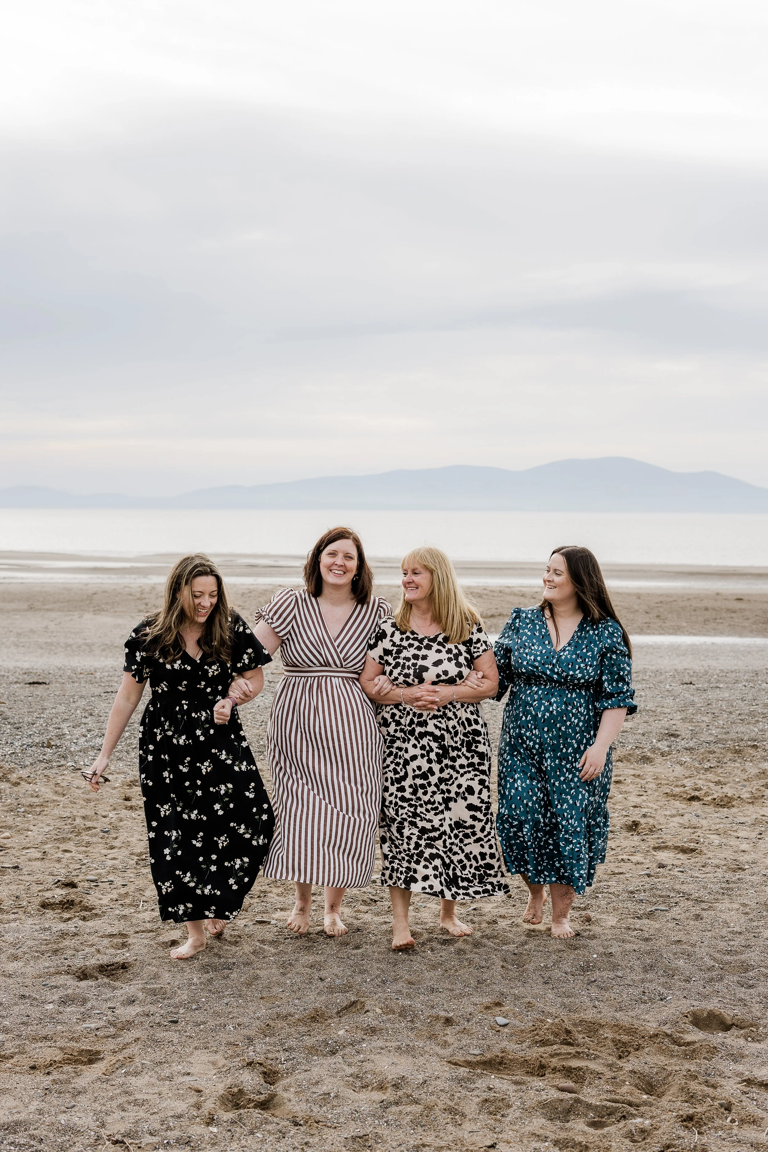 A mother and her daughters sharing a quiet moment together by the sea, capturing the love, laughter and connection that grows through every season of life.