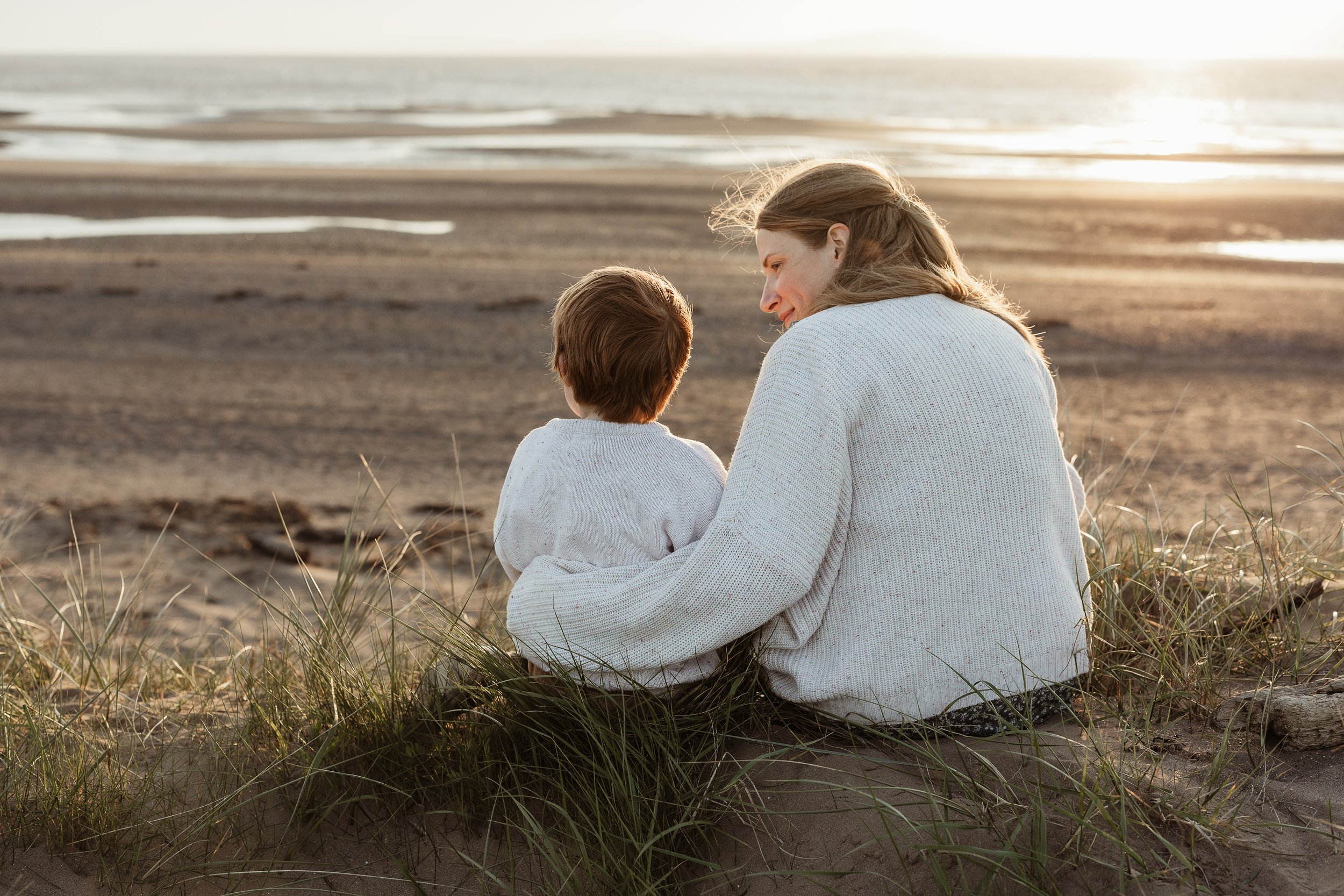 Mum and child sitting together on the beach at sunset.