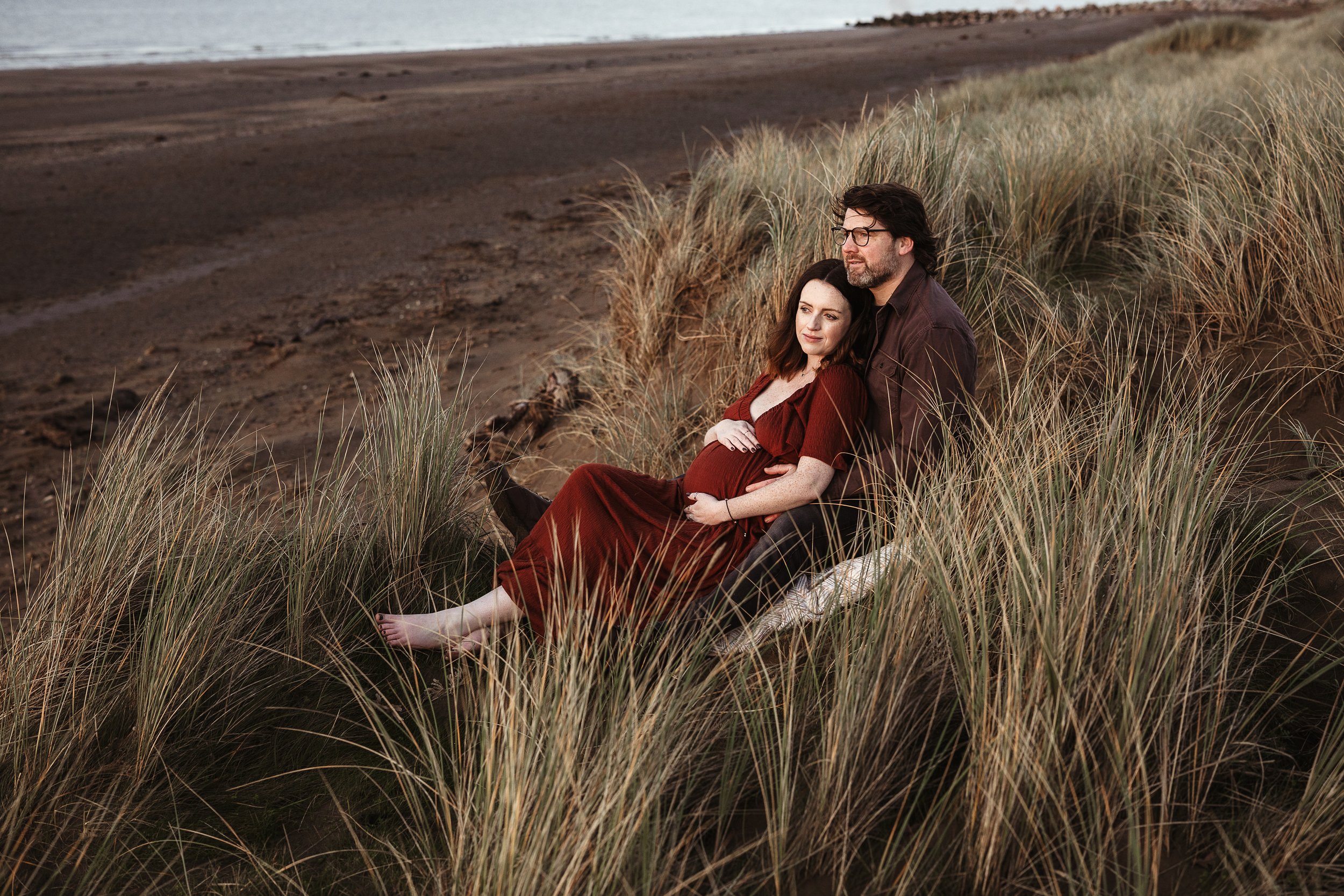Expecting parents sharing a quiet moment together by the coast during an outdoor maternity photography session.