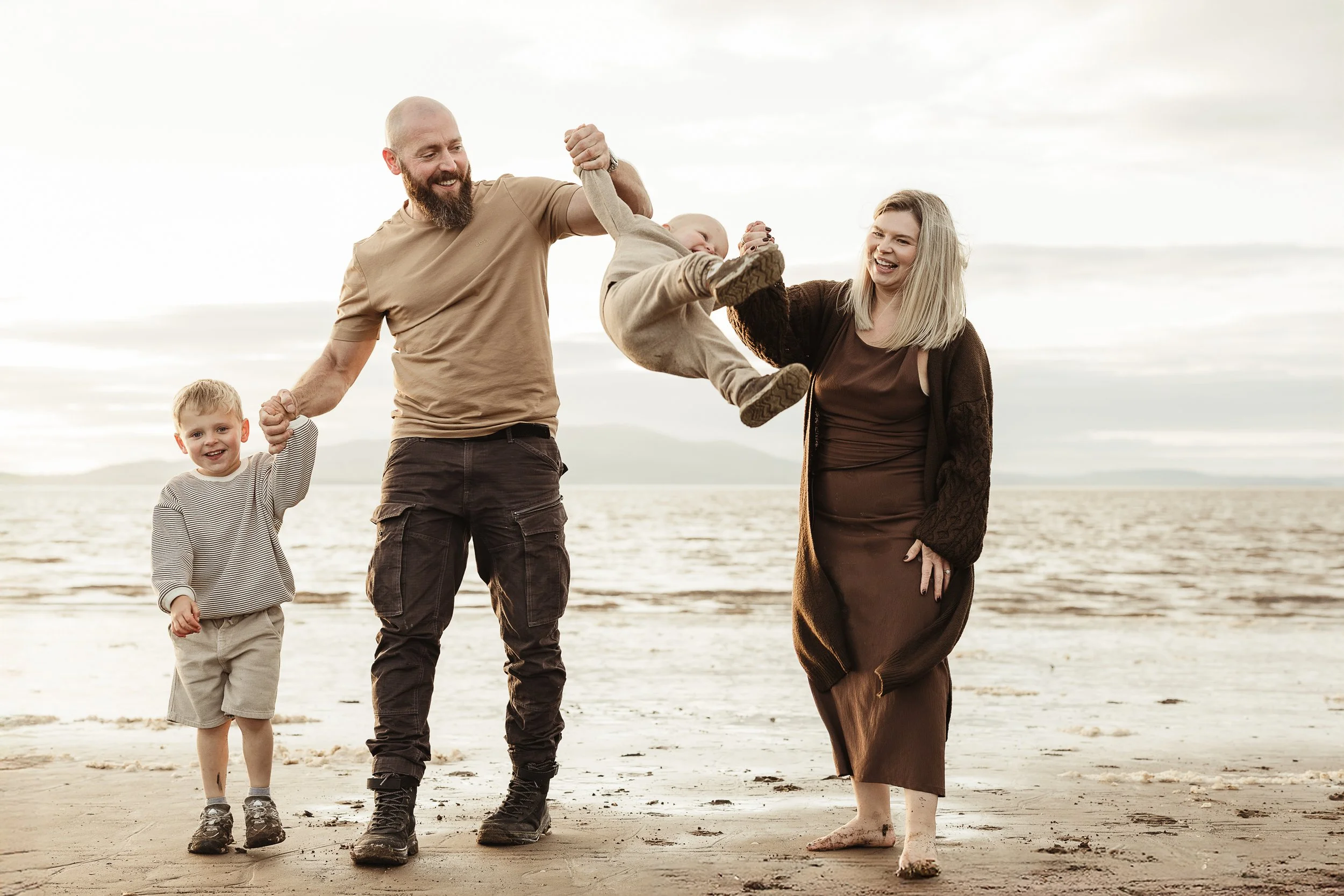 A family of four enjoying a playful beach moment together, capturing laughter, connection and the joy of childhood.