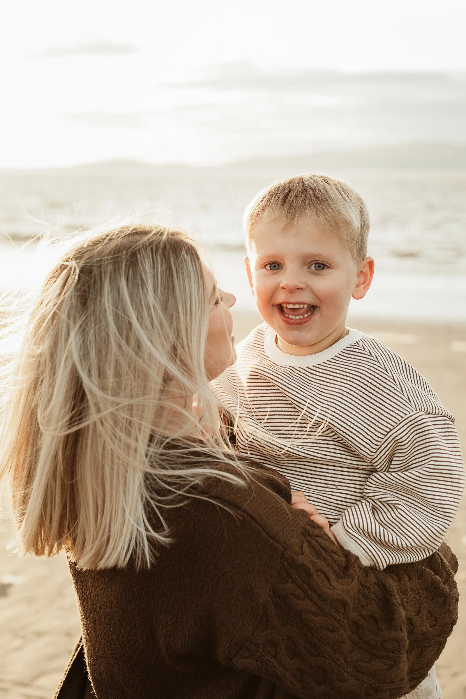 A mother and child sharing a joyful beach moment together, preserving the closeness, playfulness and bond between them.