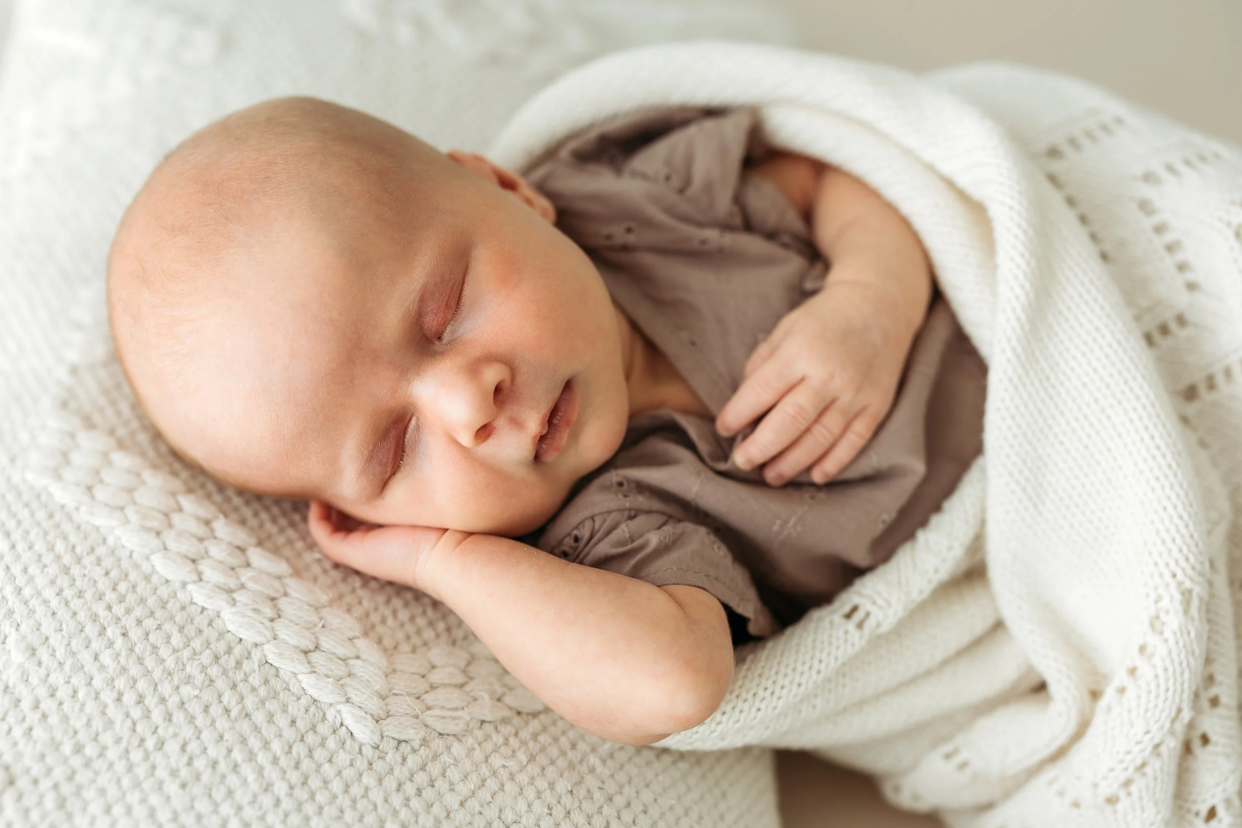 Sleeping newborn baby wrapped in a soft blanket during a natural newborn photography session.