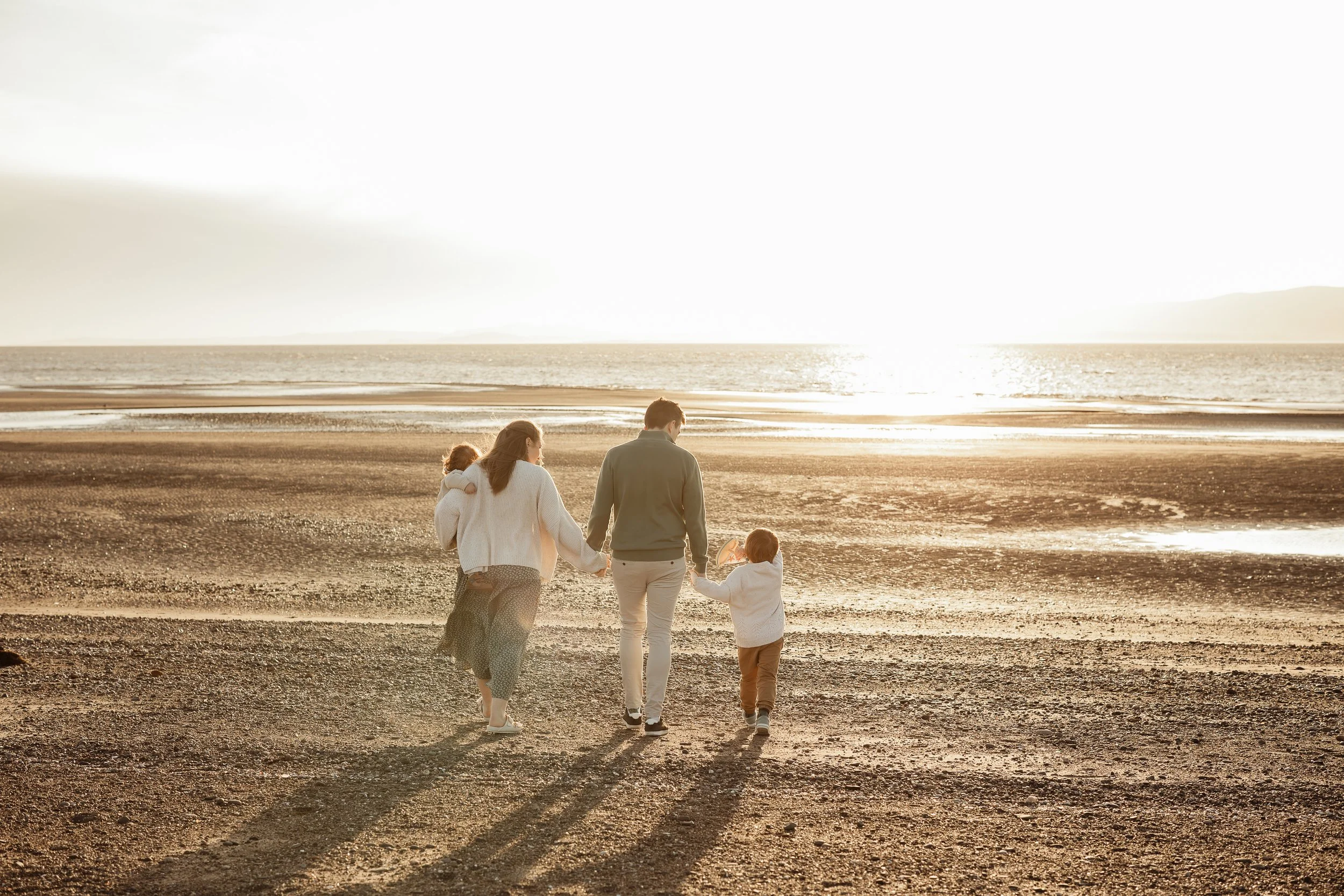 Family of four walking hand in hand along Silloth West Beach at sunset.