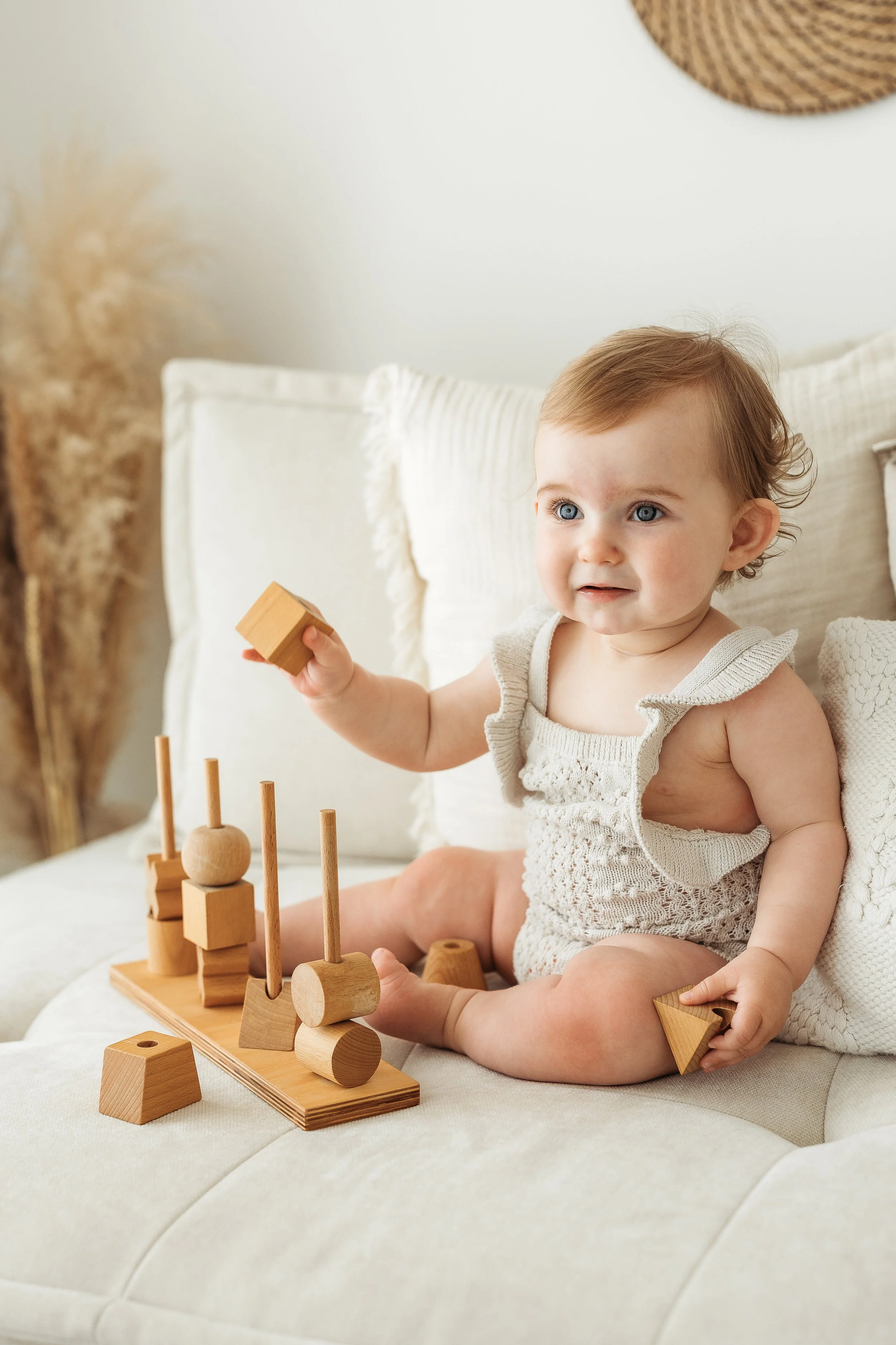 One year old child playing with wooden stacking toys on a white cushion during a relaxed first birthday photography session.